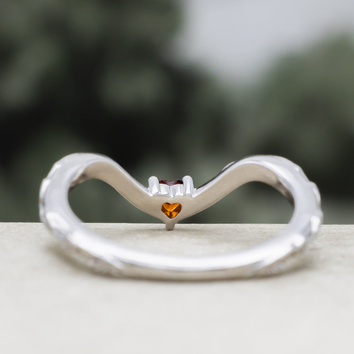 White gold heart garnet tracer with vine band against a blurred green background