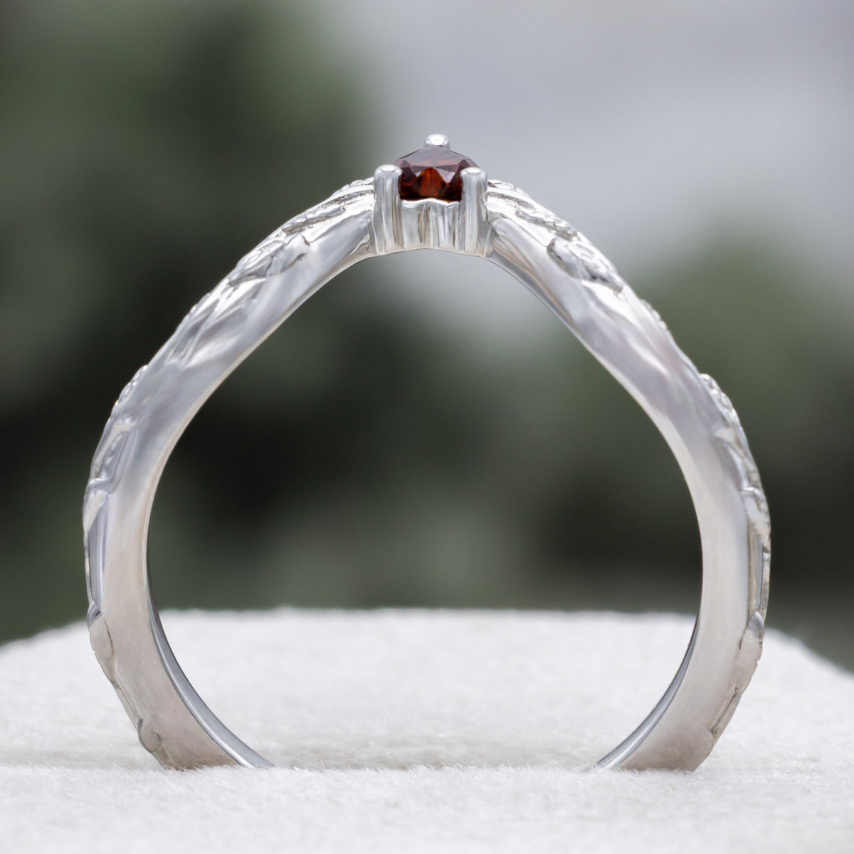 White gold heart garnet tracer with vine band against a blurred green background