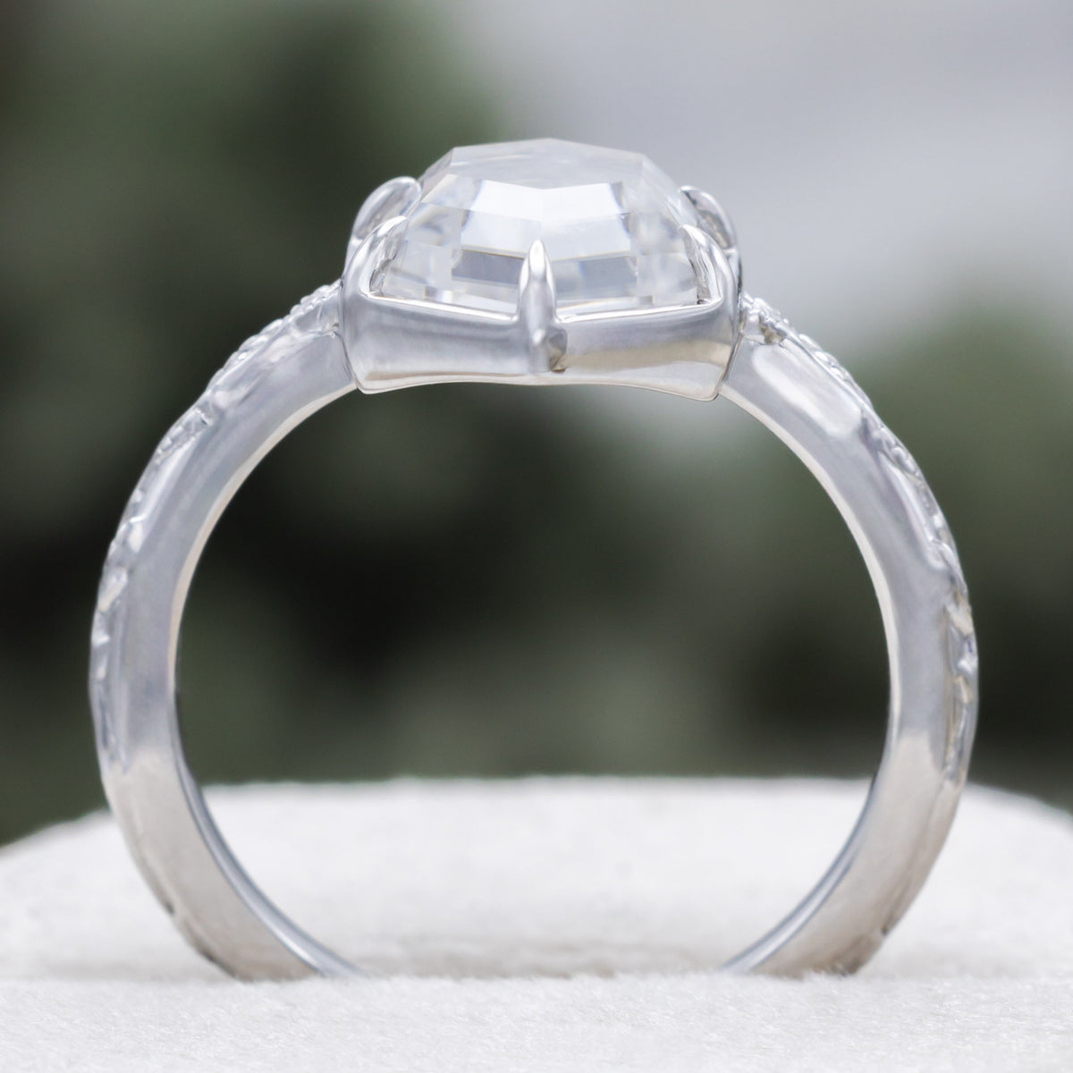 White gold engagement ring with portrait cut moissanite on vine band against a blurred green background