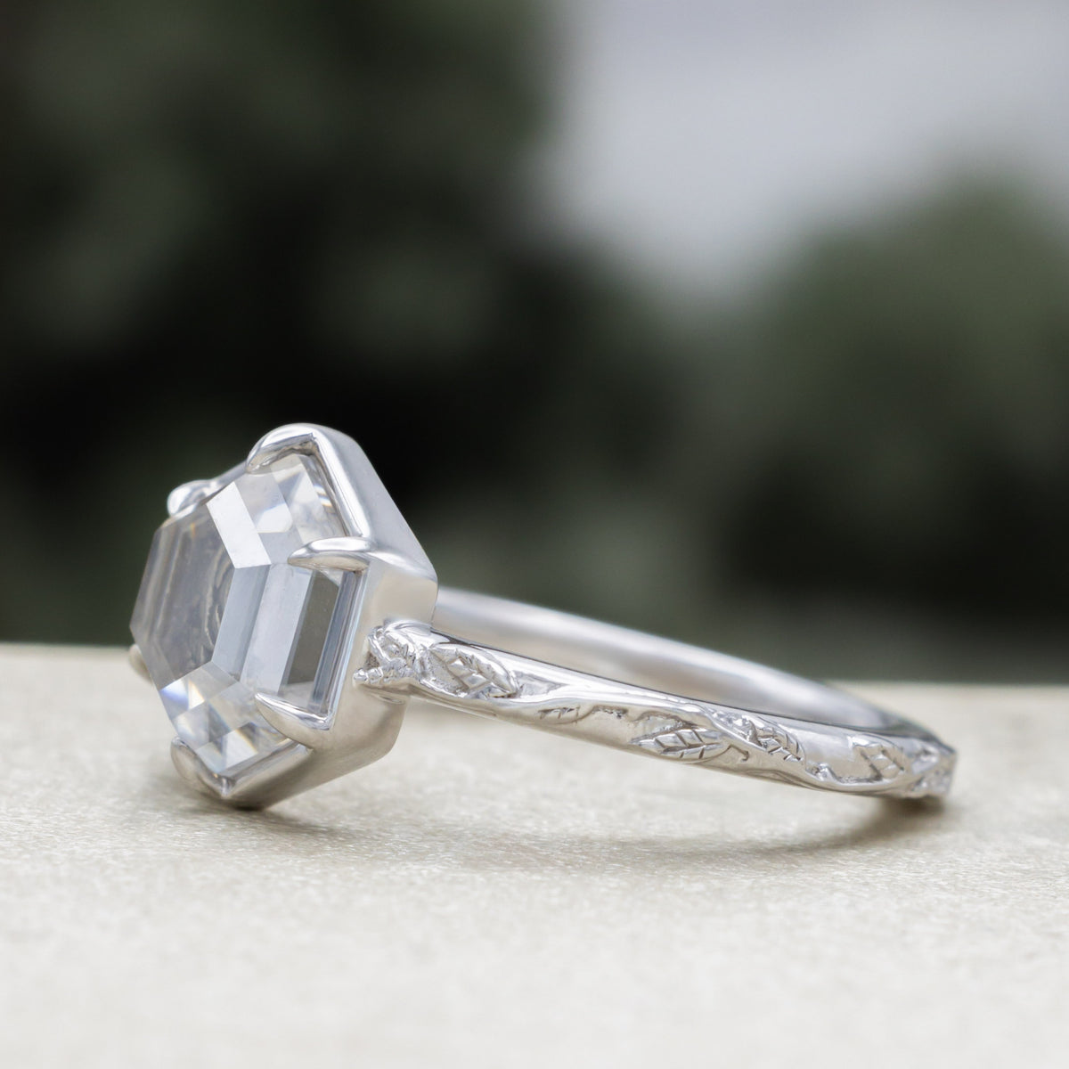 White gold engagement ring with portrait cut moissanite featuring rose design on vine band against a blurred green background