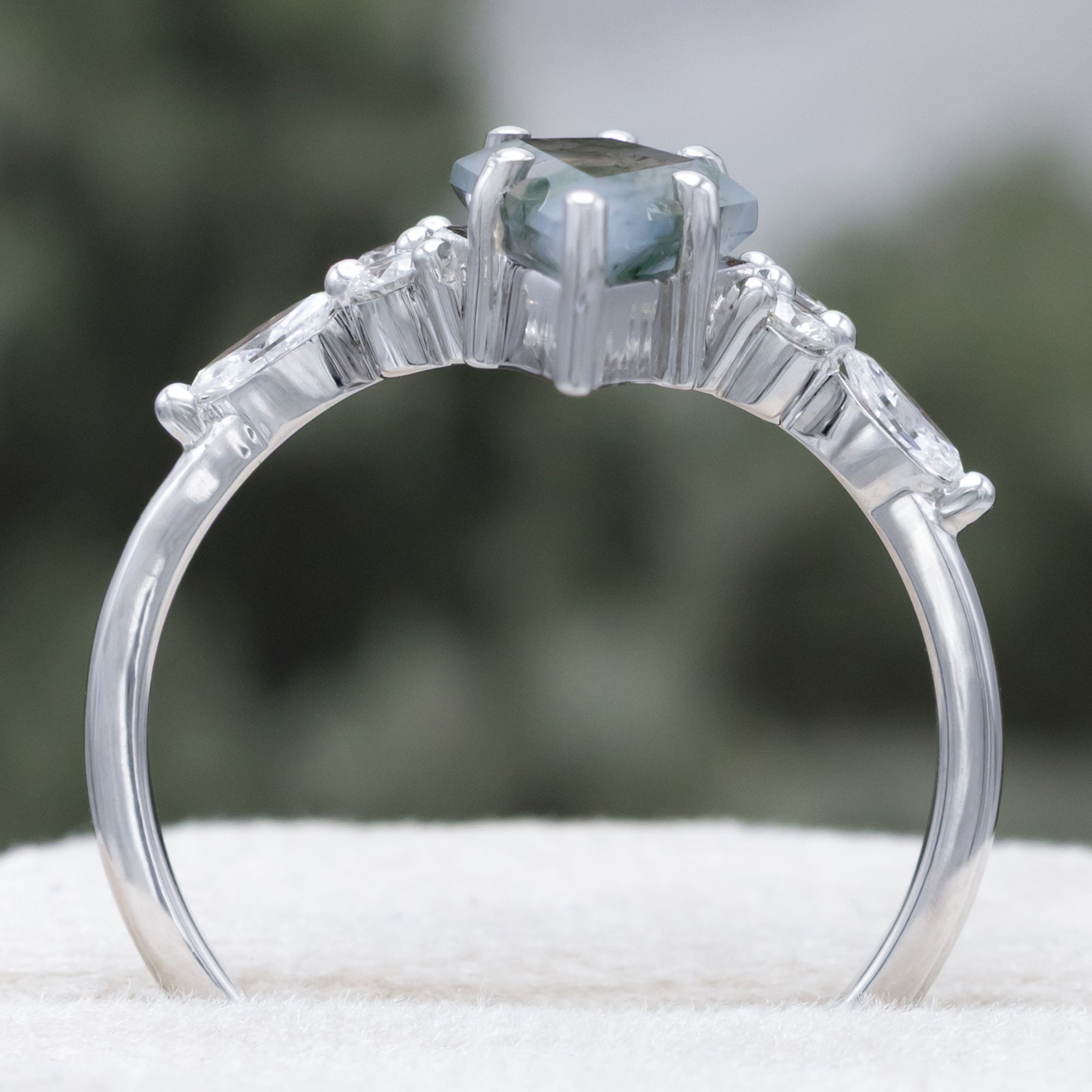 White gold ring with a moss agate center stone and diamond accents on a blurred background