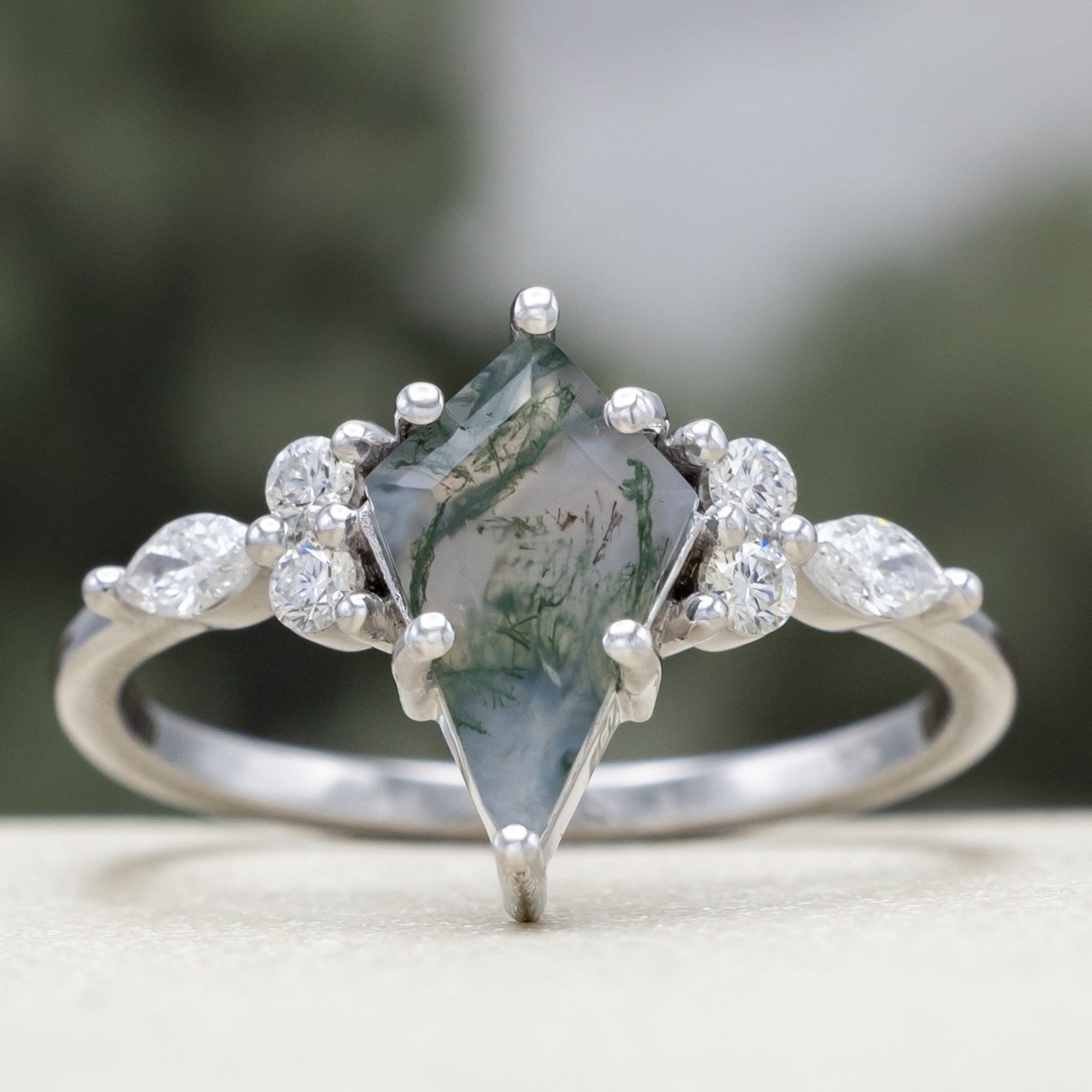 White gold ring with a moss agate center stone and diamond accents on a blurred background