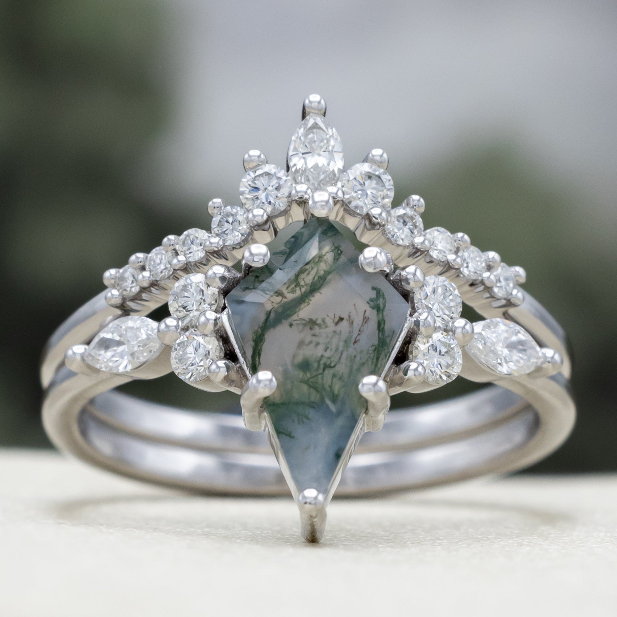 White gold ring with a moss agate center stone and diamond accents on a blurred background