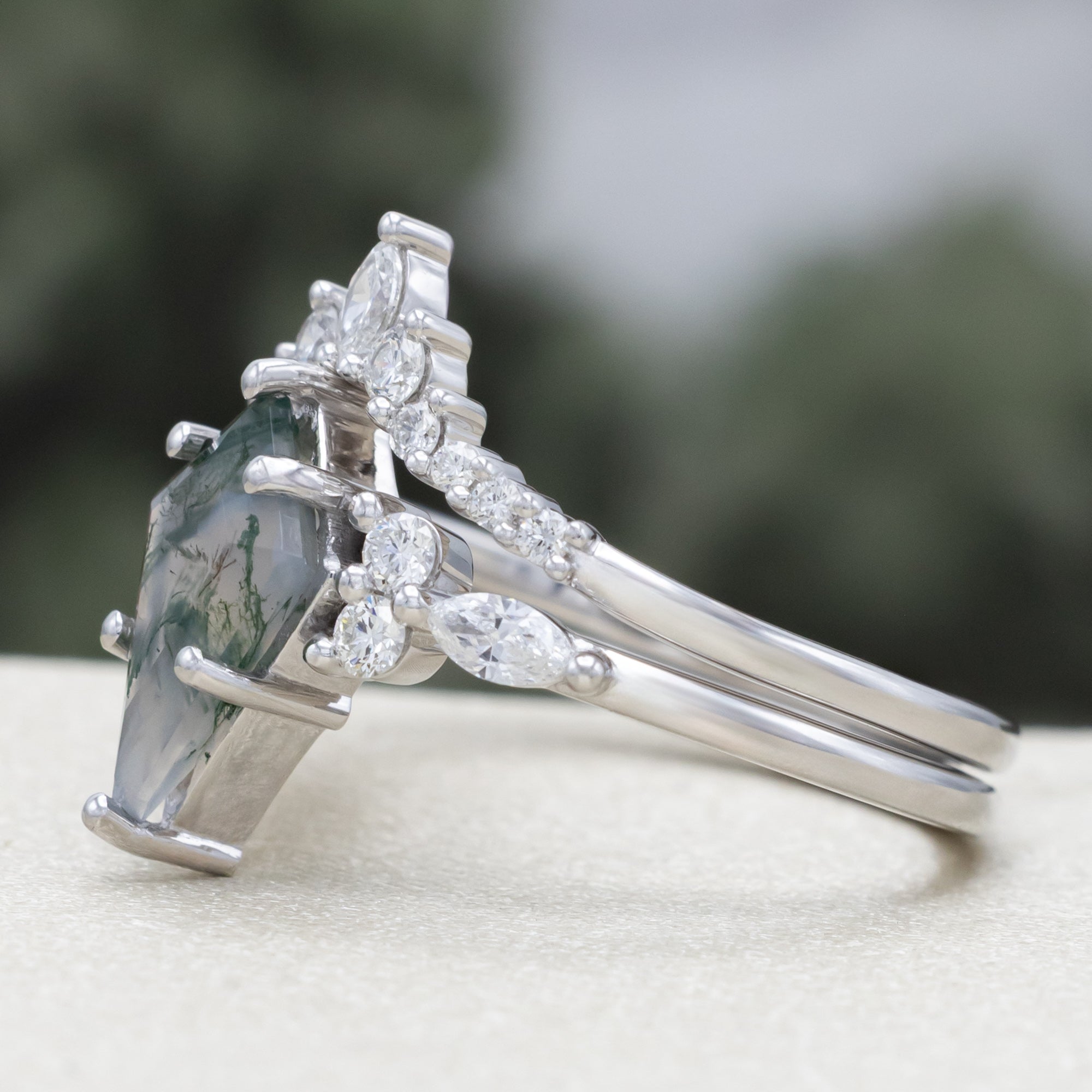 White gold ring with a moss agate center stone and diamond accents on a blurred background