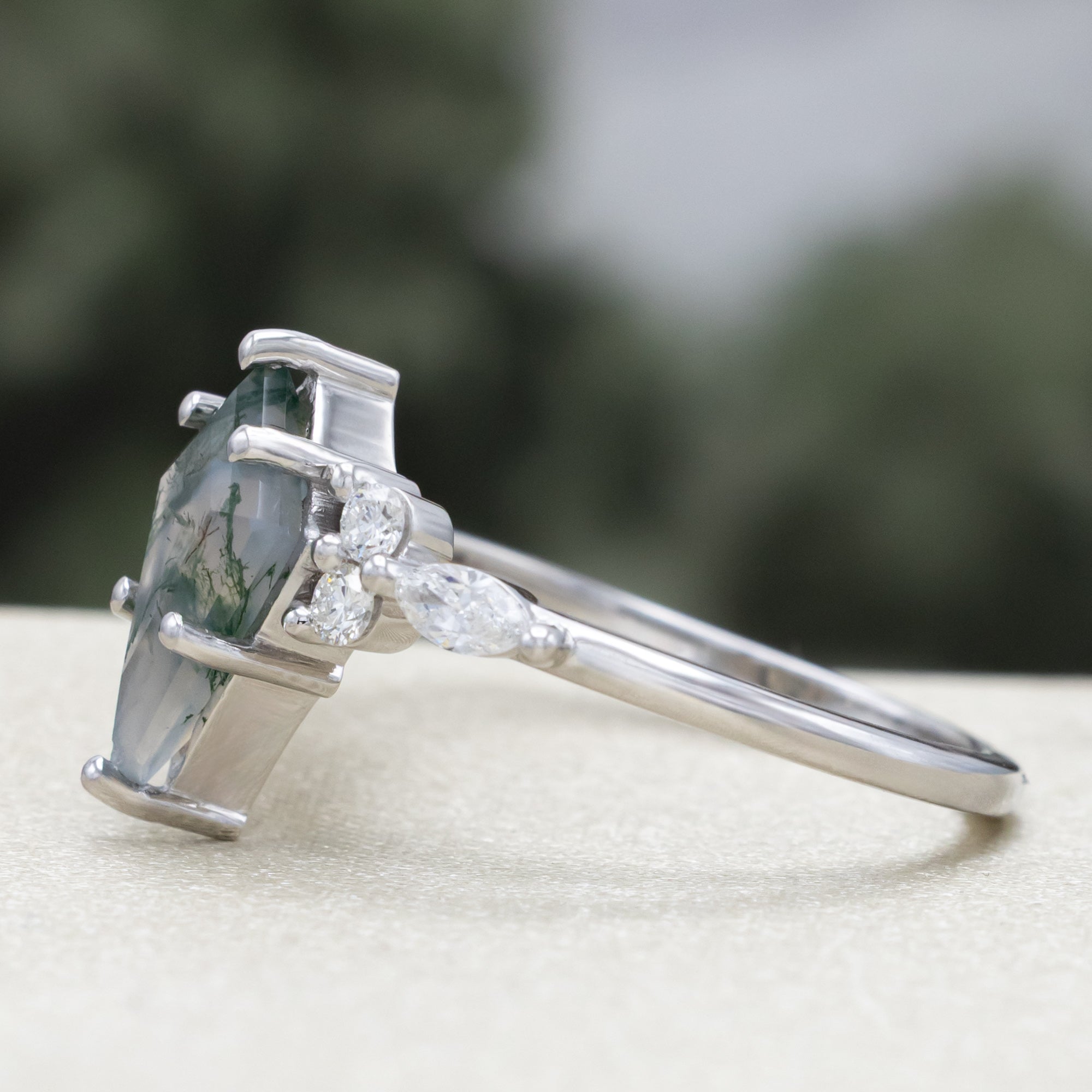 White gold ring with a moss agate center stone and diamond accents on a blurred background