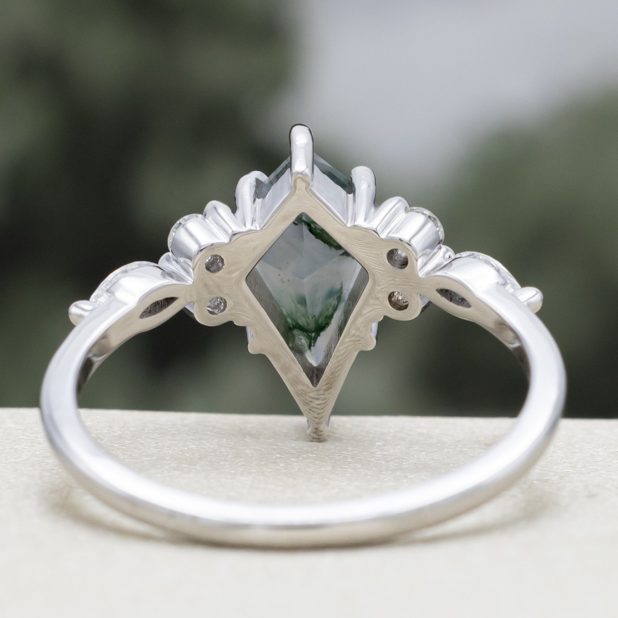 White gold ring with a moss agate center stone and diamond accents on a blurred background