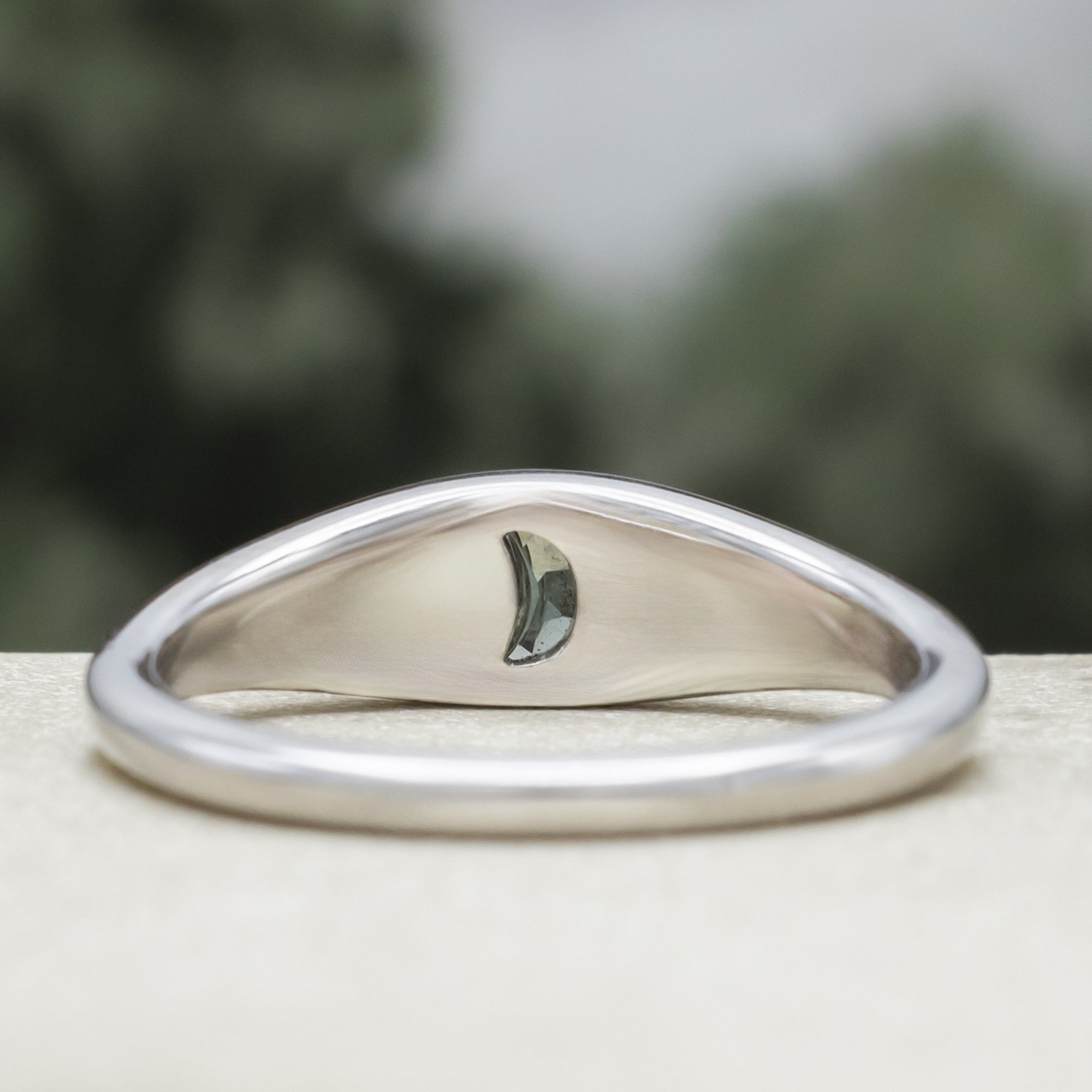 White gold ring with crescent moon shaped sapphire against a blurred green background