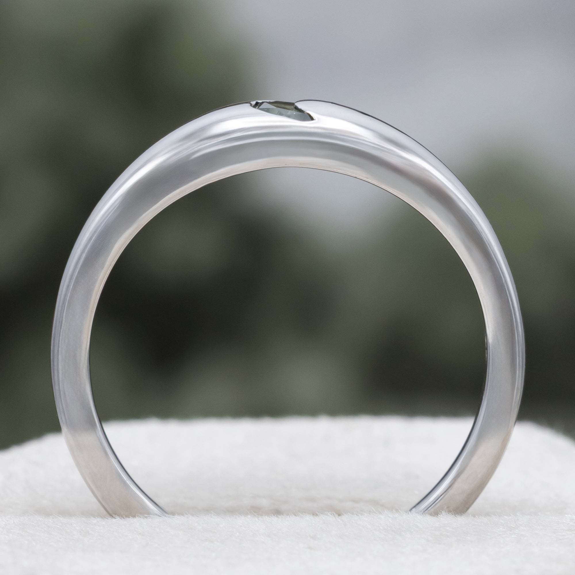 White gold ring with crescent moon shaped sapphire against a blurred green background