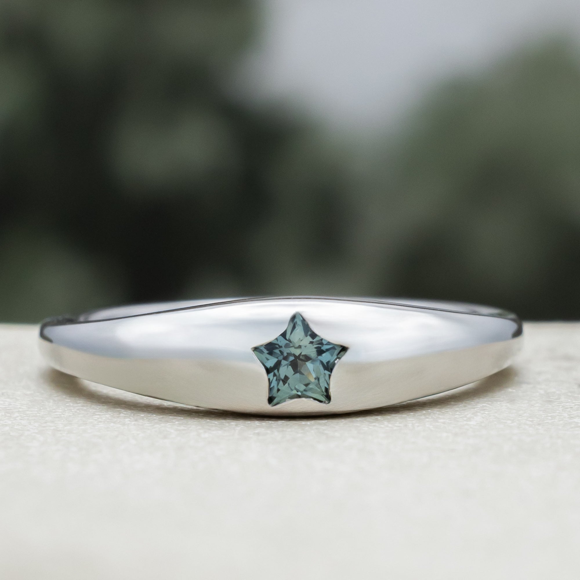 White gold ring with star shaped sapphire against a blurred green background
