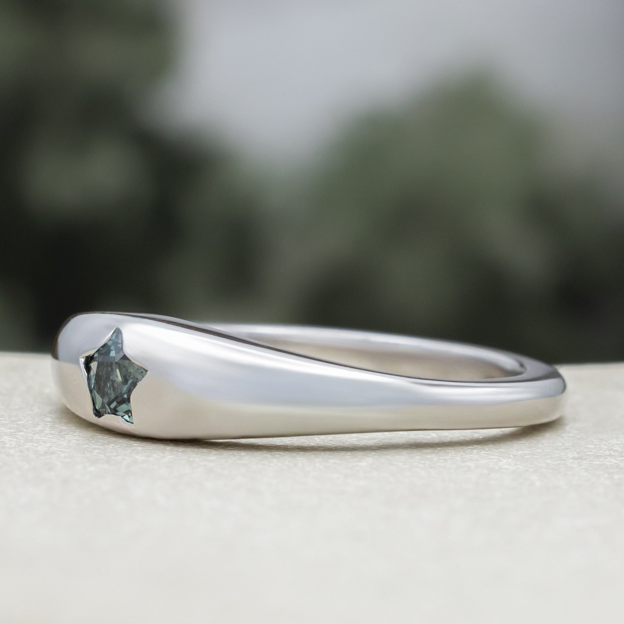 White gold ring with star shaped sapphire against a blurred green background