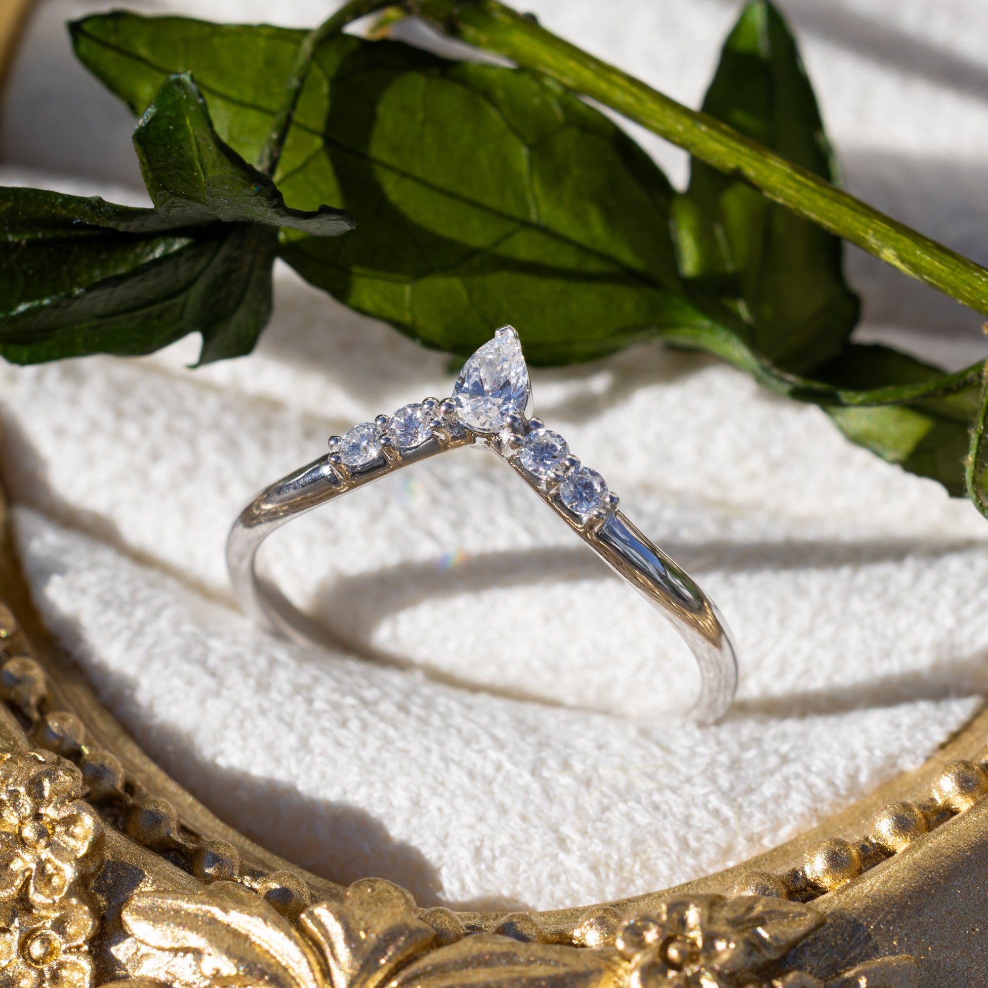 White gold ring with diamond accents on a white surface with green leaves in the background