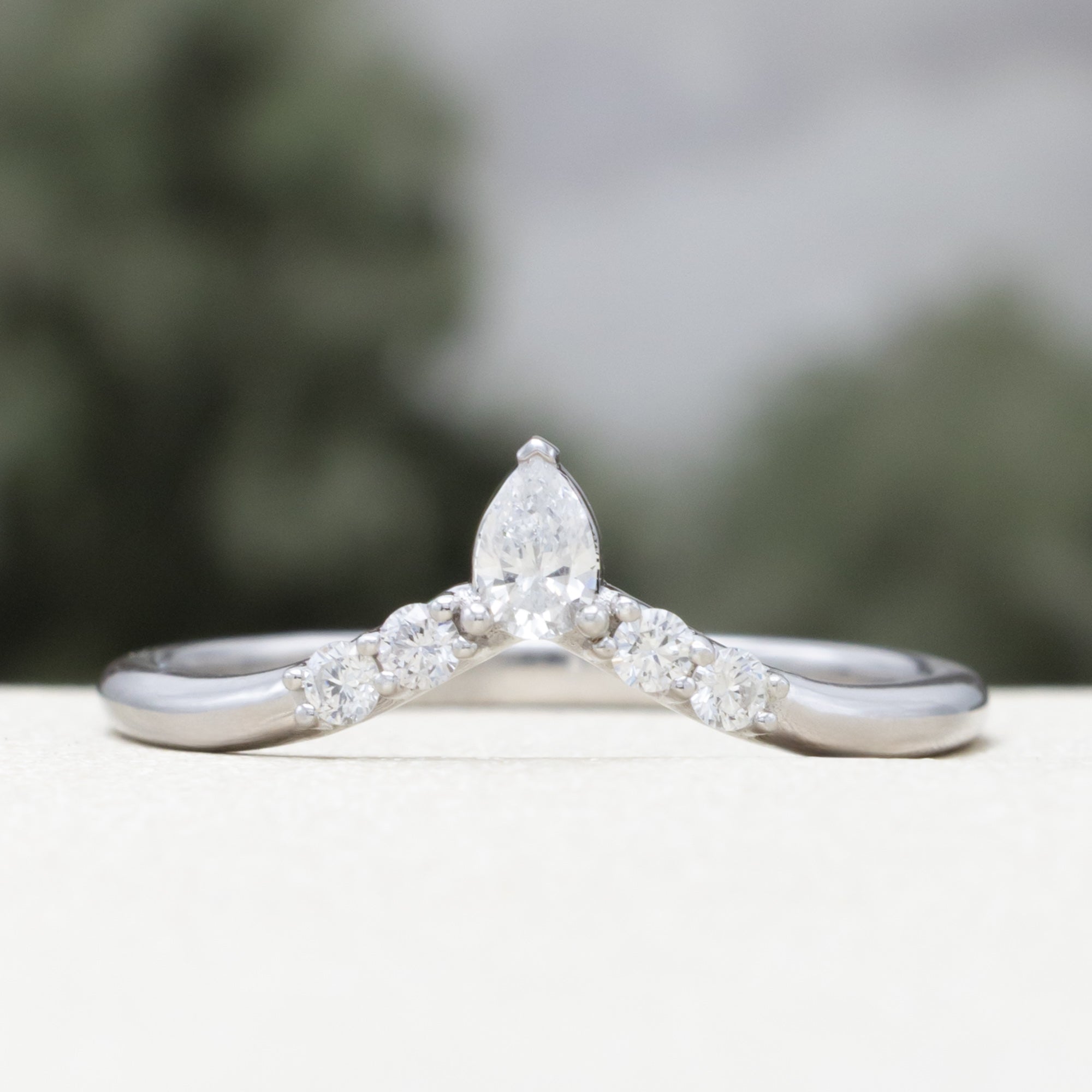 White gold ring with diamond accents on a blurred natural background