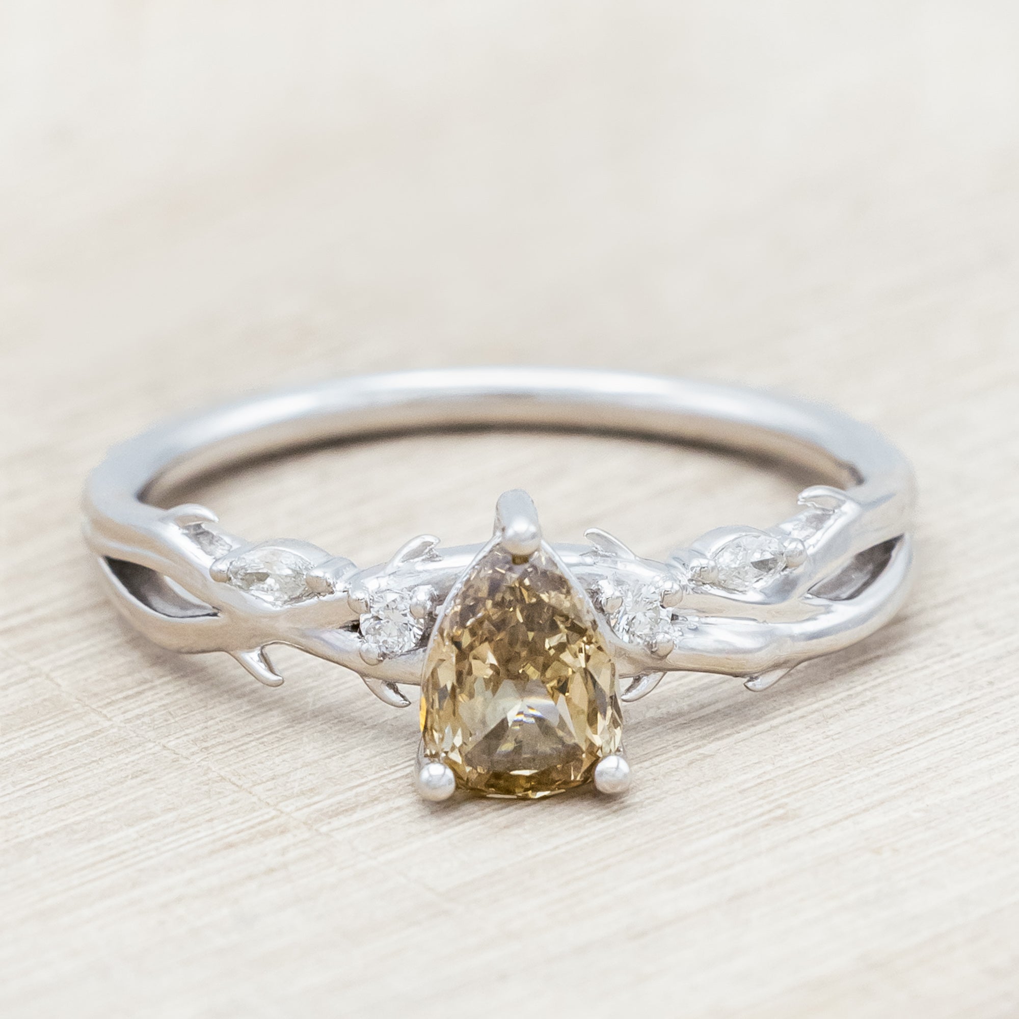 White gold ring with a pear-cut champagne diamond on a wooden stand against a beige background