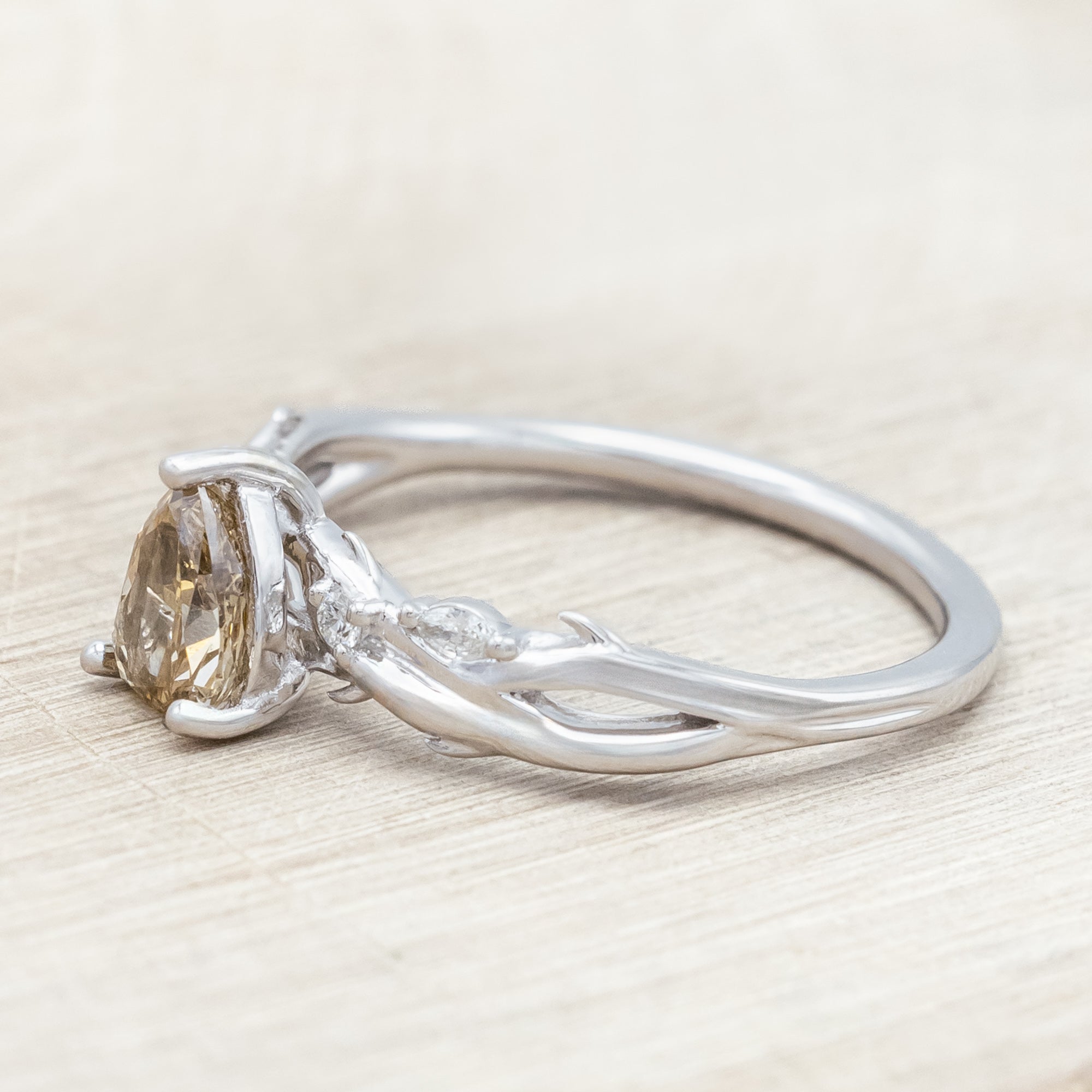 White gold ring with a pear-cut champagne diamond on a wooden stand against a beige background