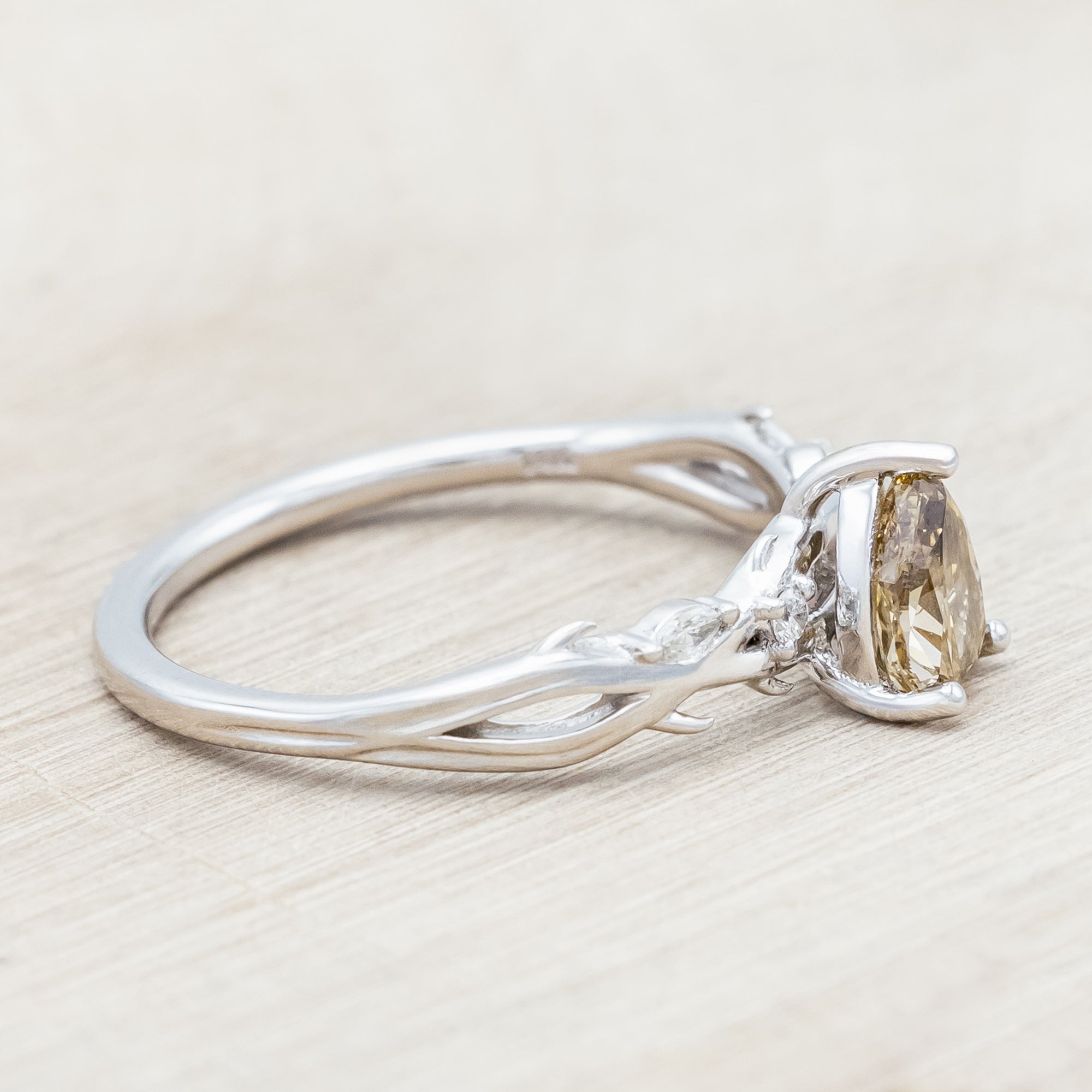 White gold ring with a pear-cut champagne diamond on a wooden stand against a beige background