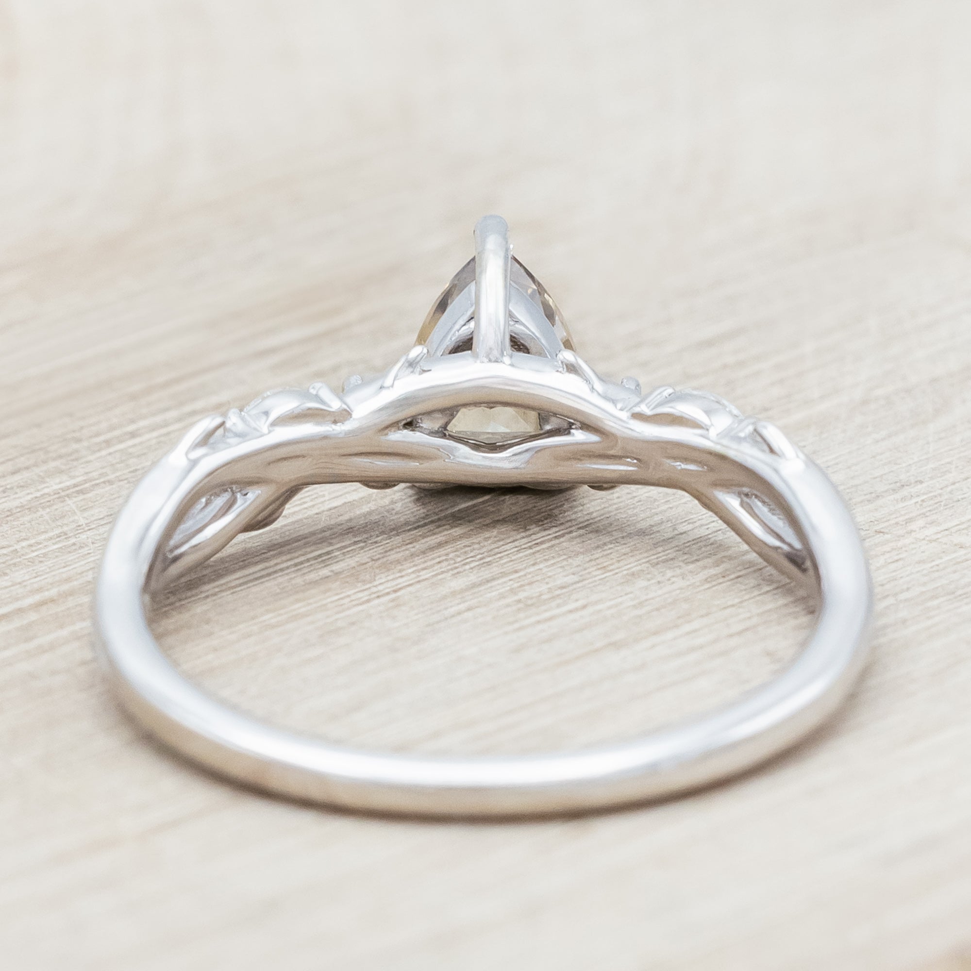 White gold ring with a pear-cut champagne diamond on a wooden stand against a beige background