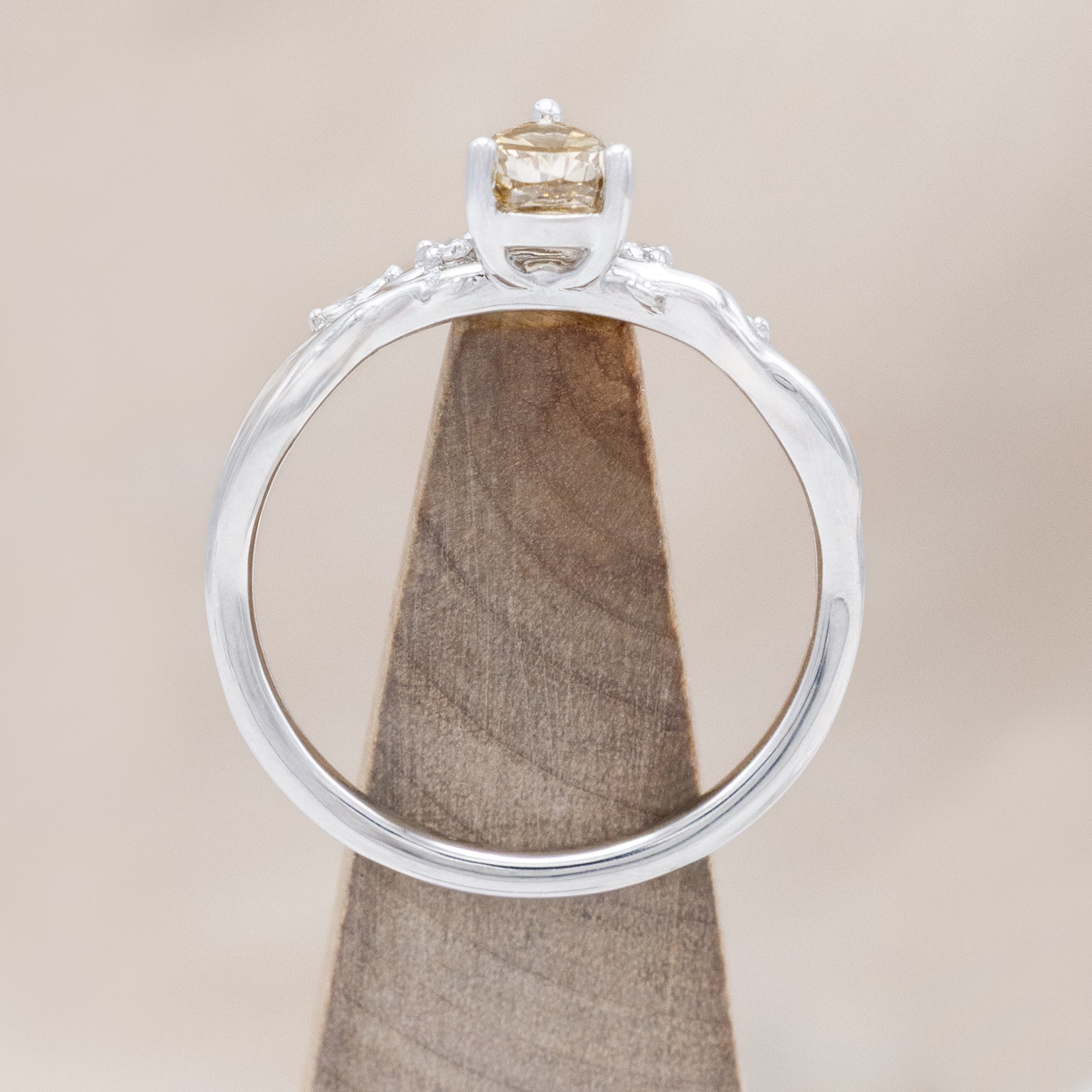 White gold ring with a pear-cut champagne diamond on a wooden stand against a beige background