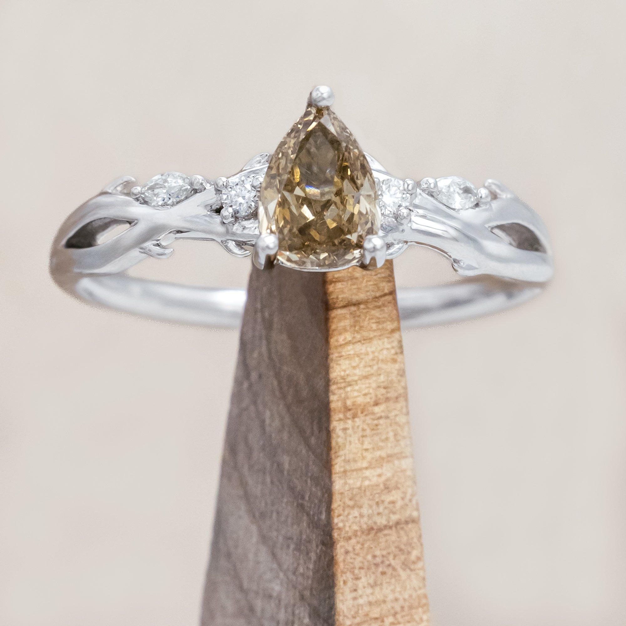 White gold ring with a pear-cut champagne diamond on a wooden stand against a beige background