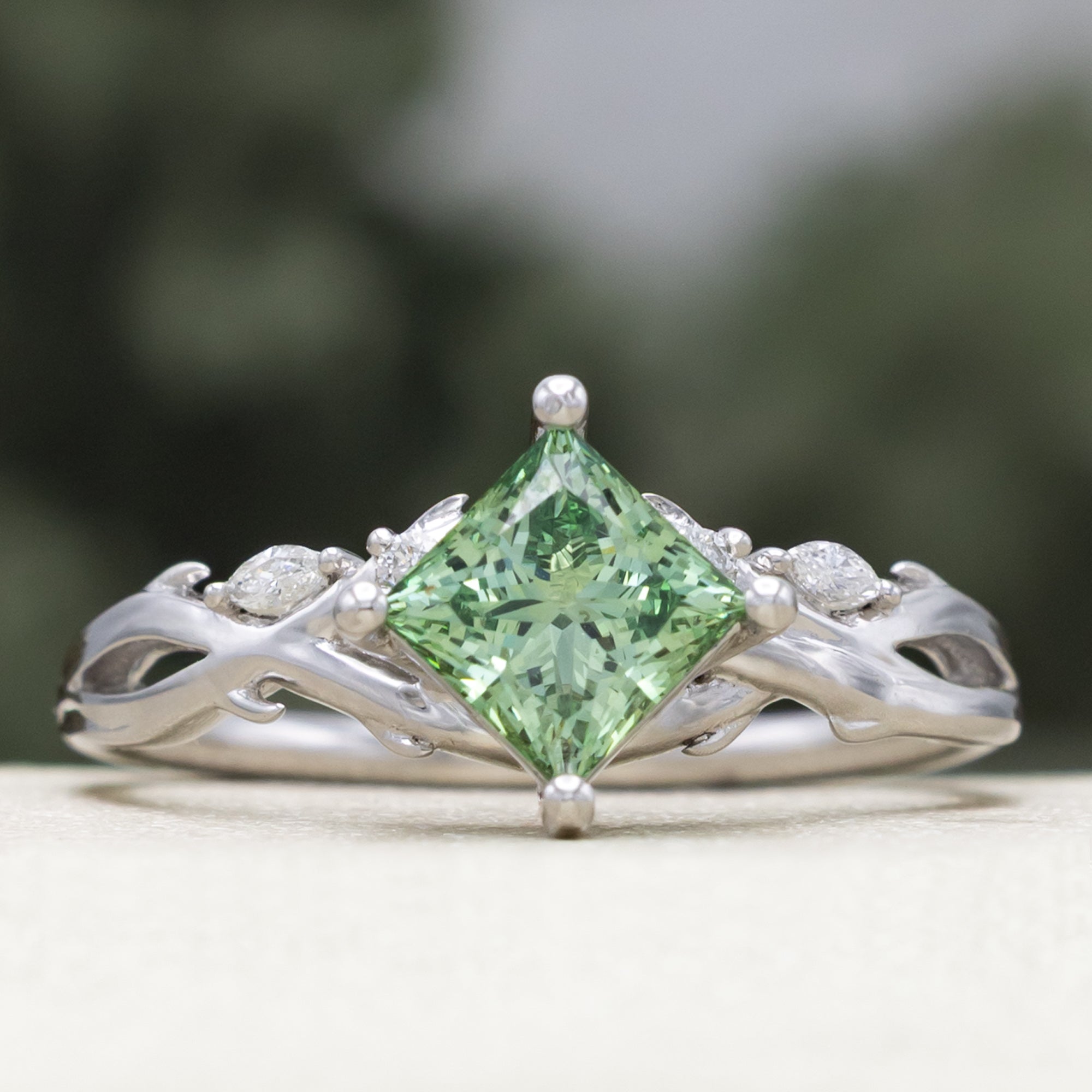 White gold ring with a green lab diamond on a blurred background