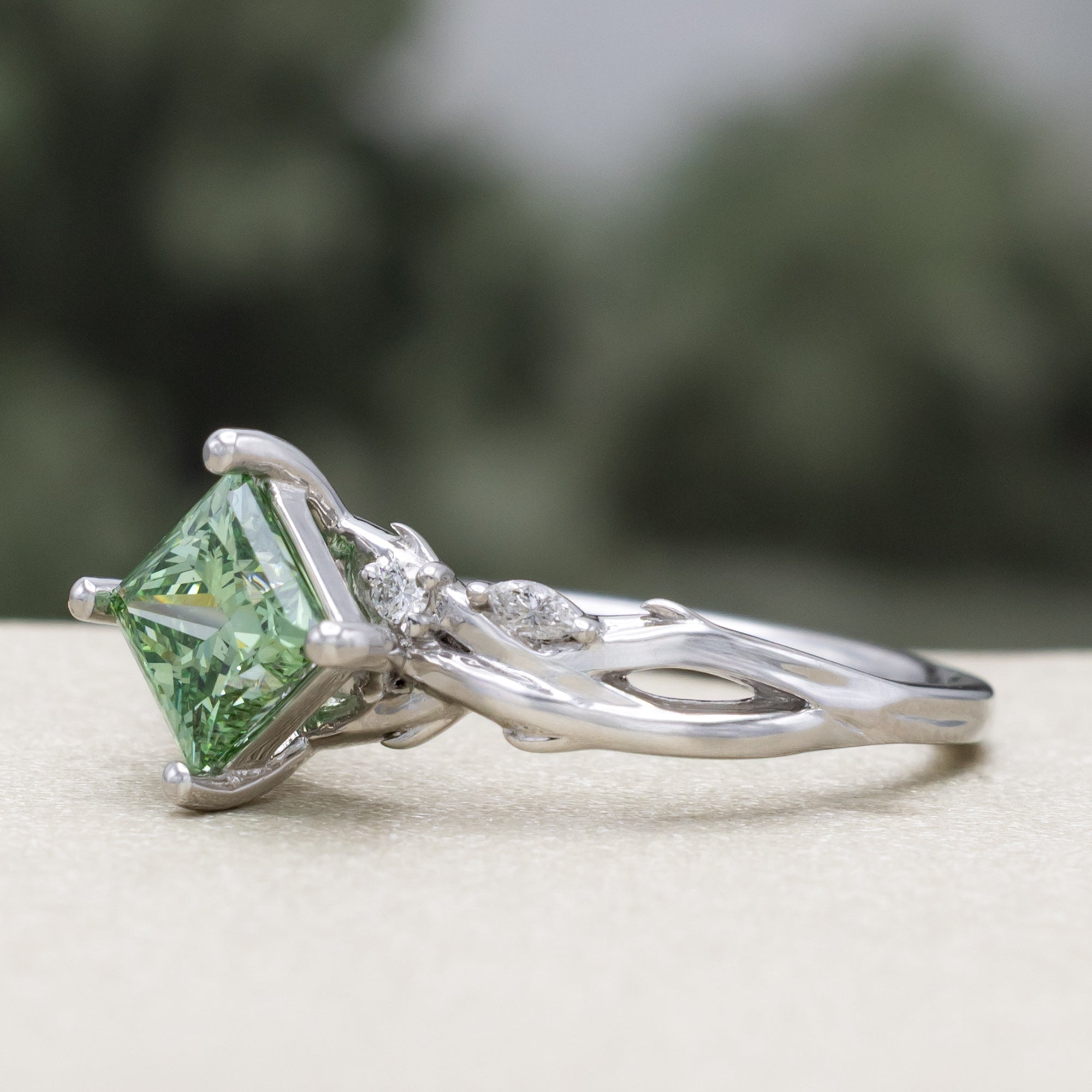 White gold ring with a green lab diamond on a blurred background