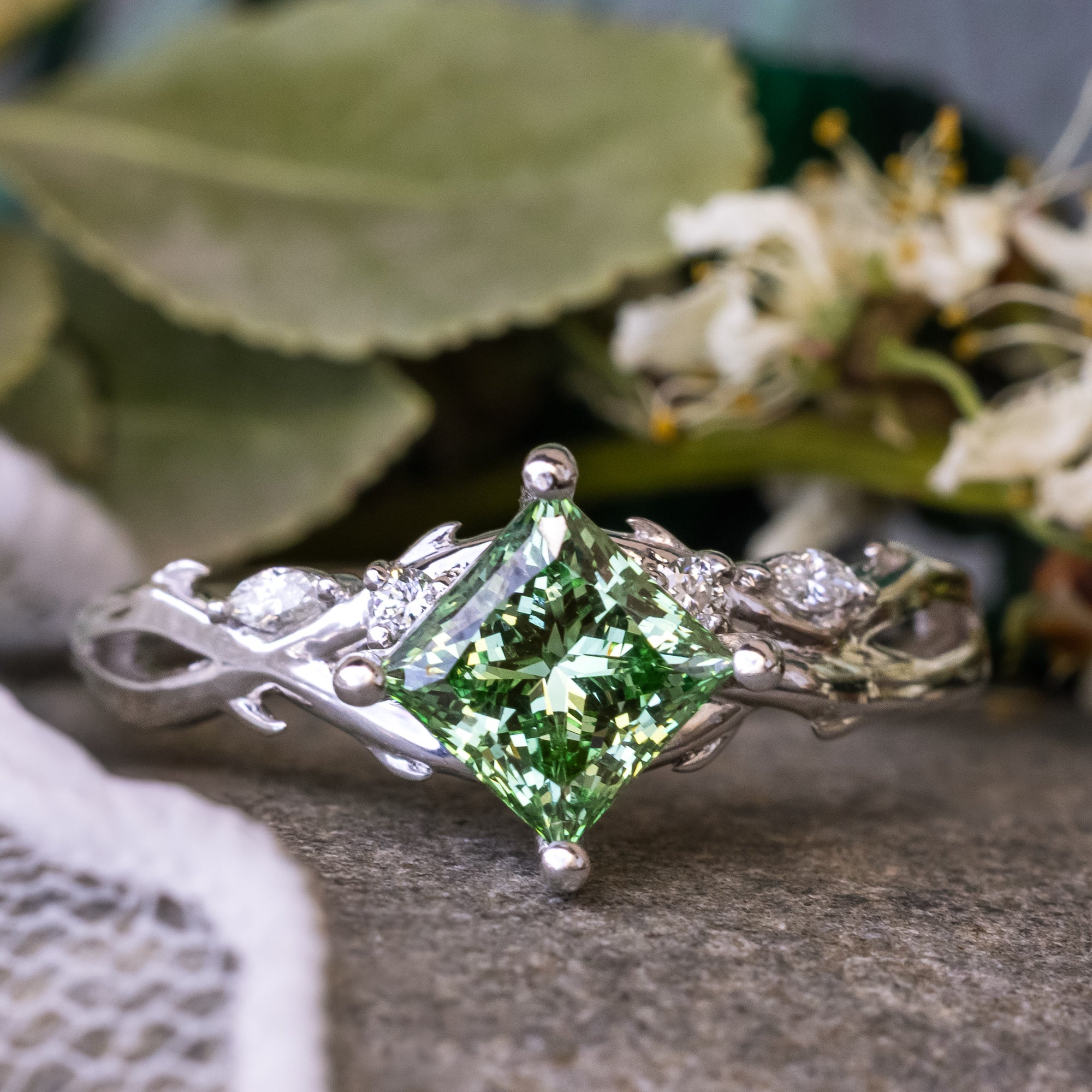 White gold ring with green lab diamond behind a floral background