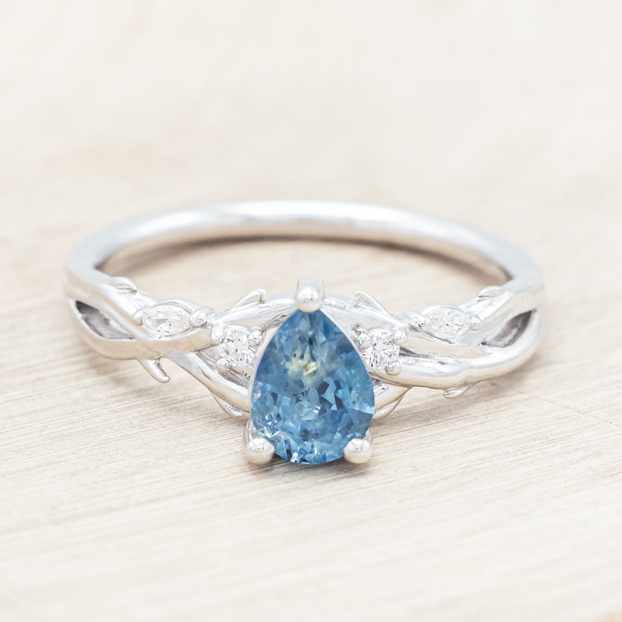 14K white gold ring with a pear Montana sapphire on a wooden stand against a beige background