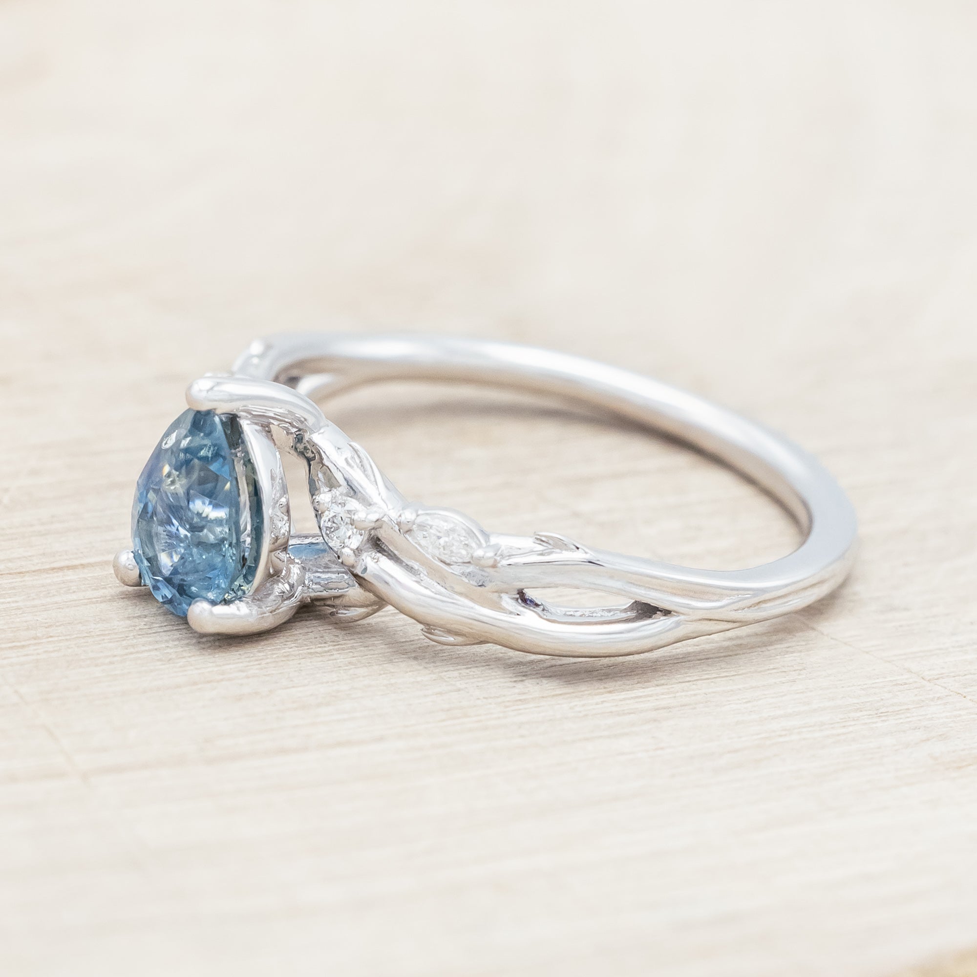 14K white gold ring with a pear Montana sapphire on a wooden stand against a beige background
