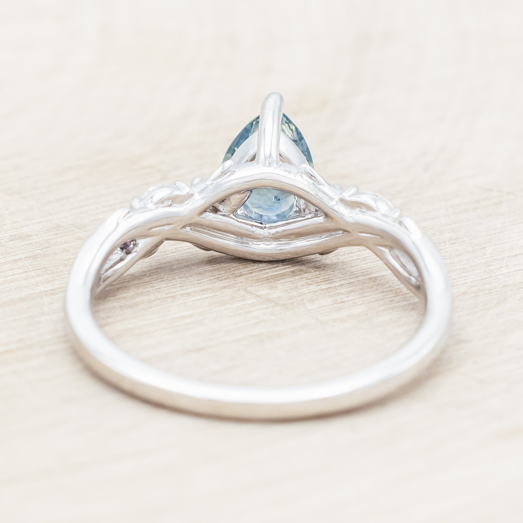 14K white gold ring with a pear Montana sapphire on a wooden stand against a beige background