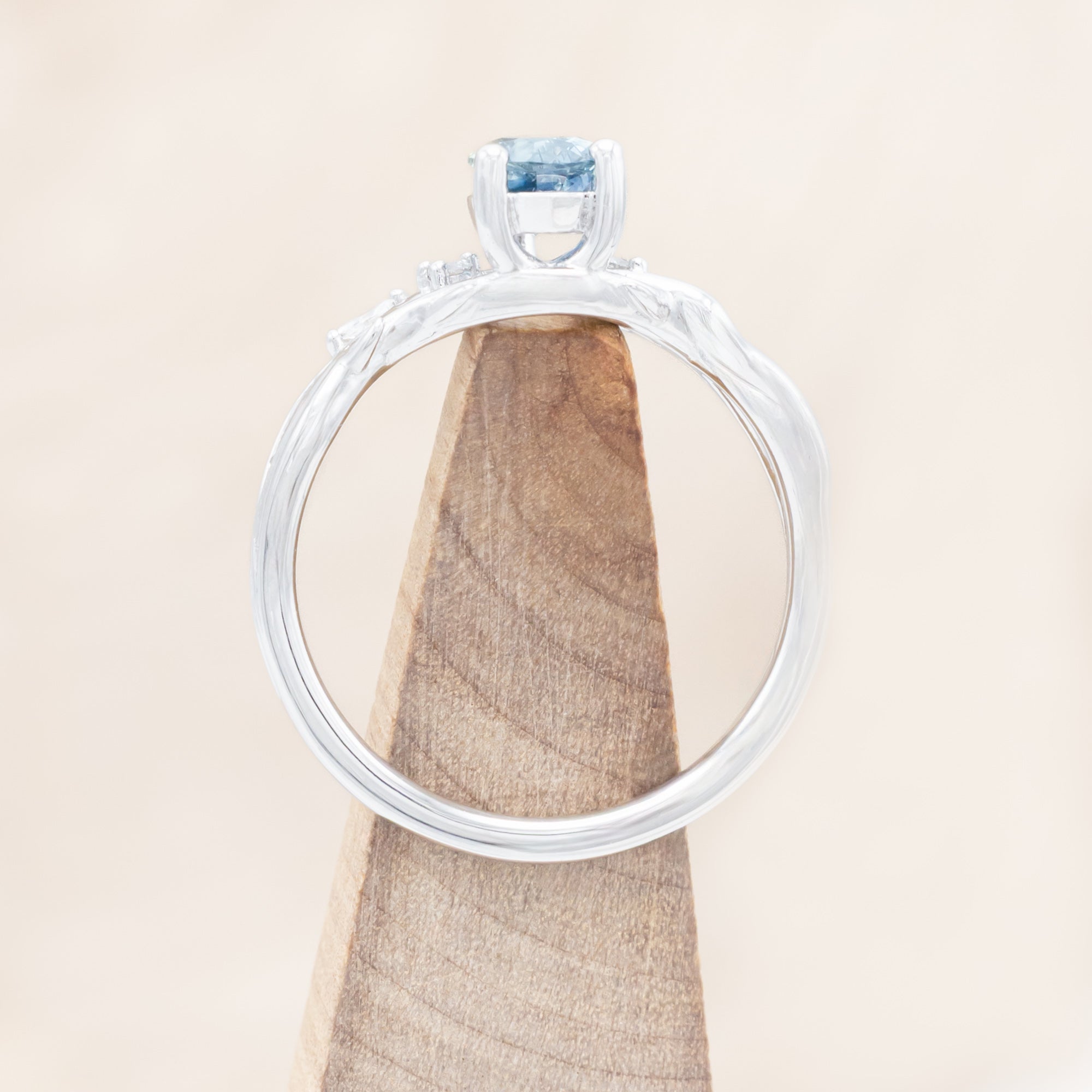 14K white gold ring with a pear Montana sapphire on a wooden stand against a beige background