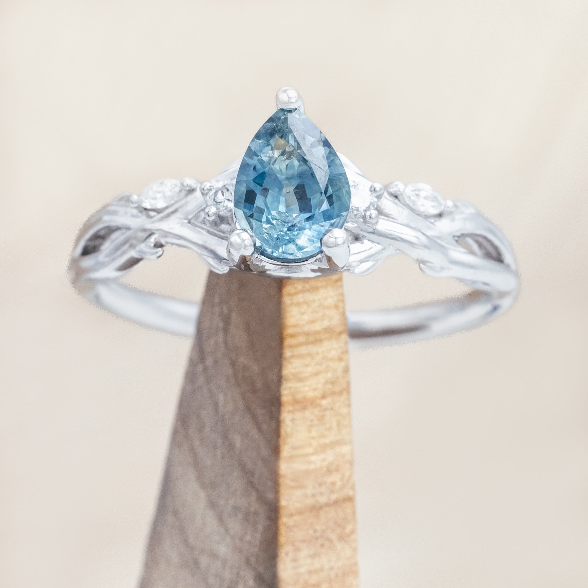 14K white gold ring with a pear Montana sapphire on a wooden stand against a beige background