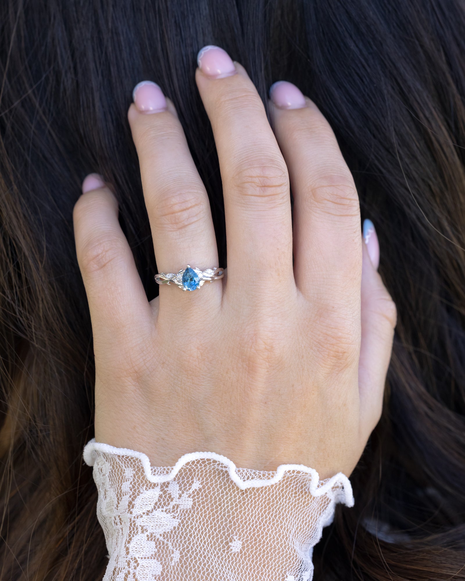 Hand wearing a ring with a blue sapphire, set against dark hair.