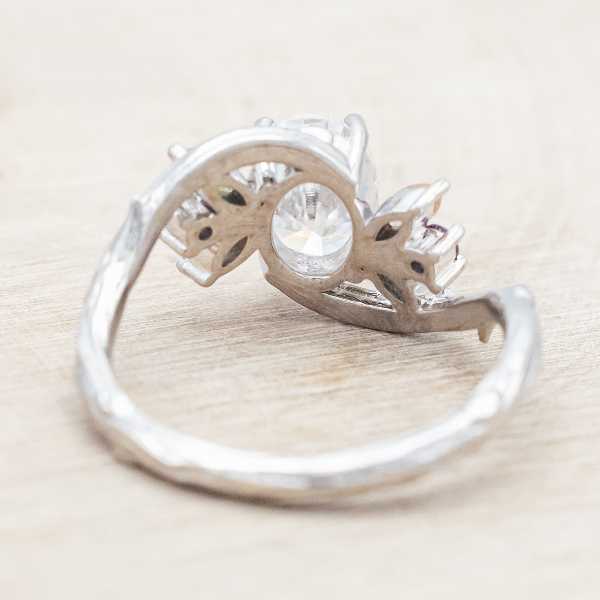 White gold ring with moissanite and smaller spinel, moss agate and sunstone accents on a wooden surface