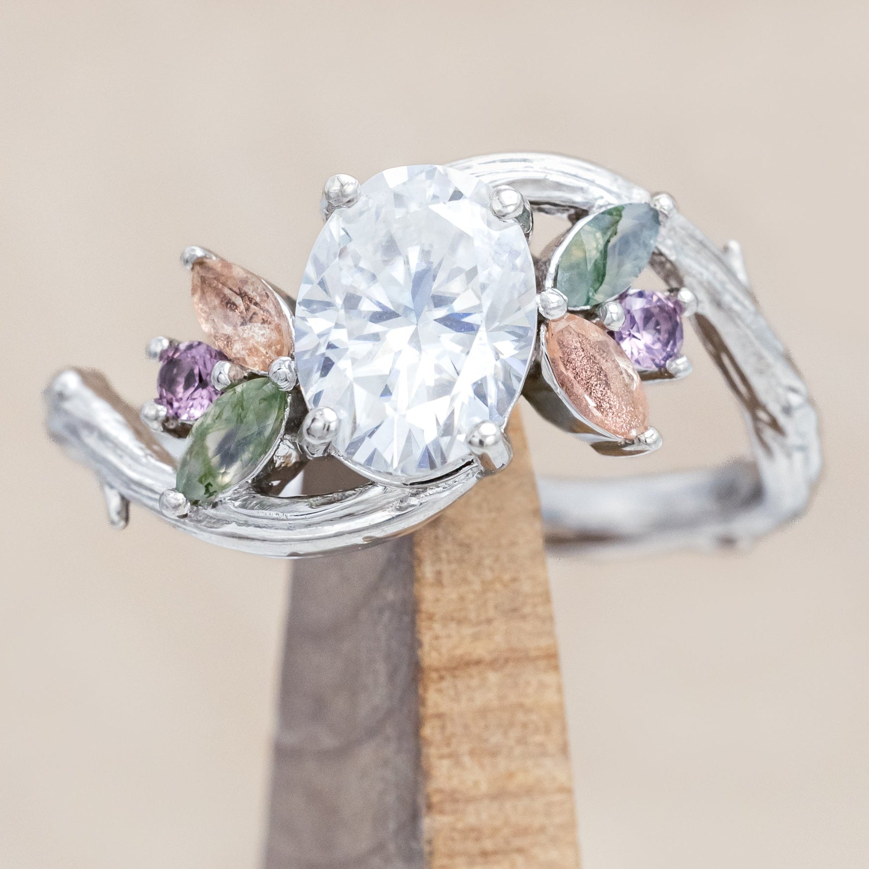 White gold ring with moissanite and smaller spinel, moss agate and sunstone accents on a wooden surface