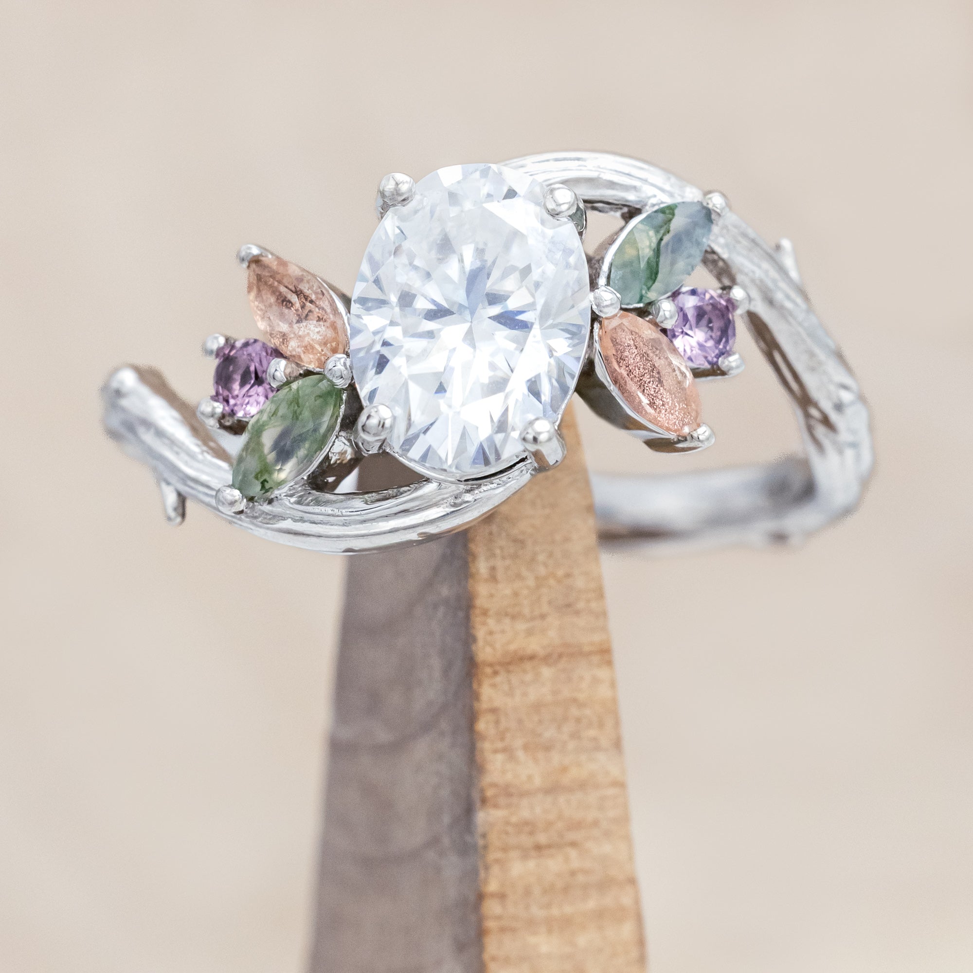 White gold ring with moissanite and smaller spinel, moss agate and sunstone accents on a wooden surface