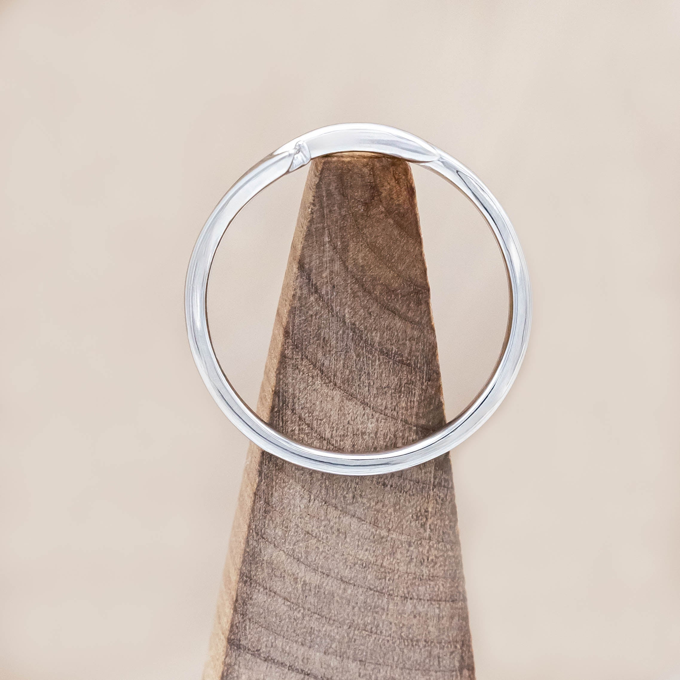 White gold ring with round diamond on a wooden stand on beige background