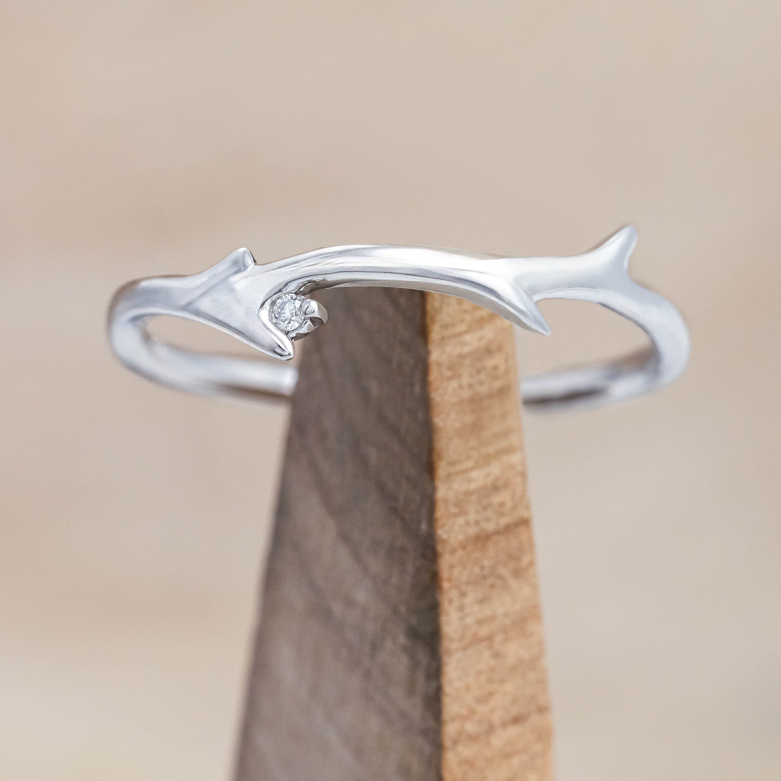 White gold ring with round diamond on a wooden stand against a beige background