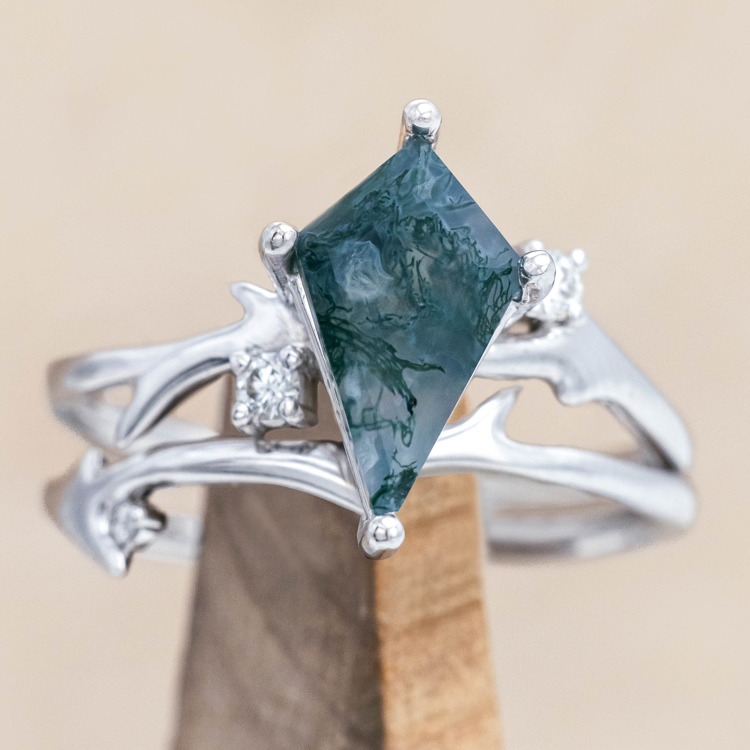 White gold ring with kite cut green moss agate on a wooden stand against a beige background 