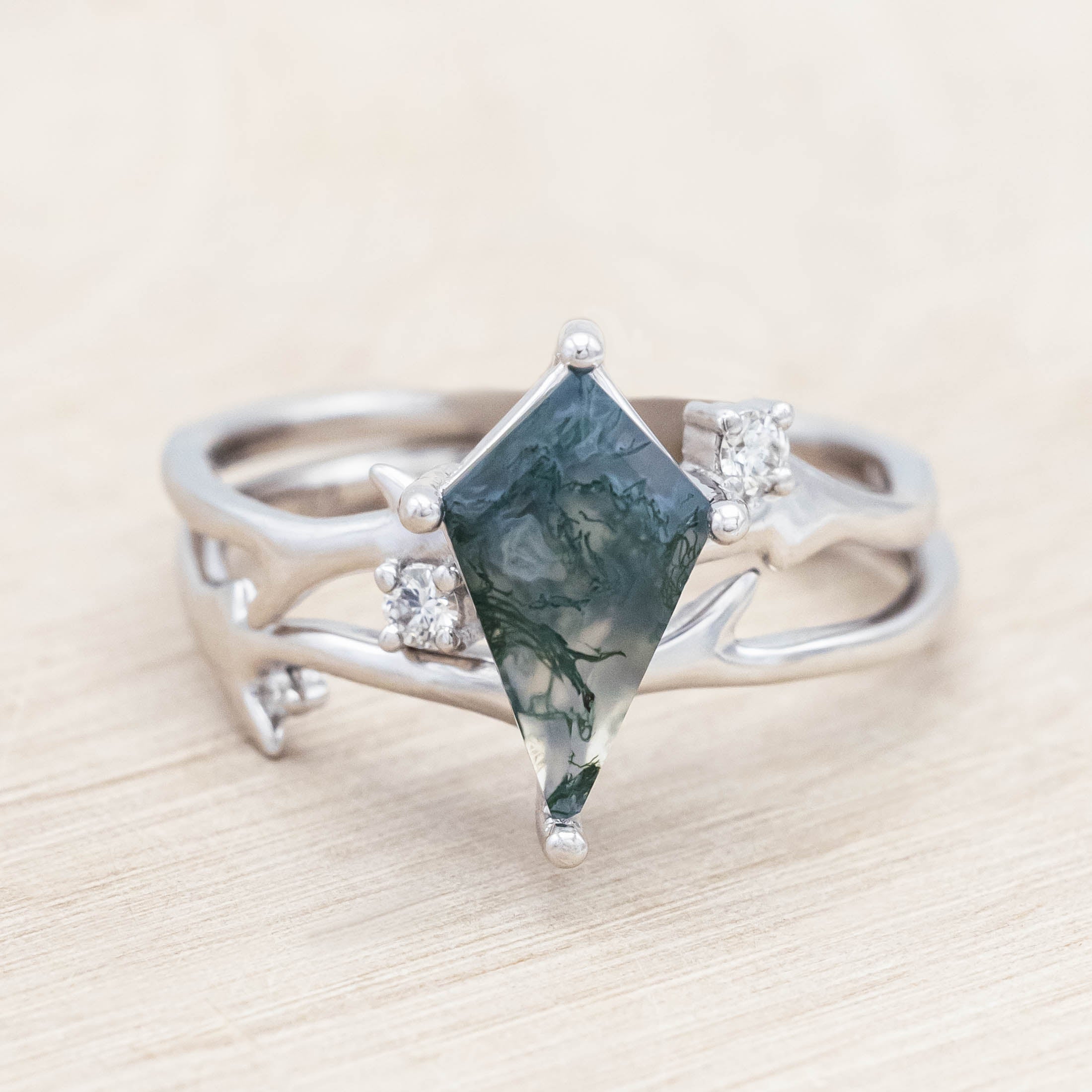White gold ring with kite cut green moss agate on a light wooden surface