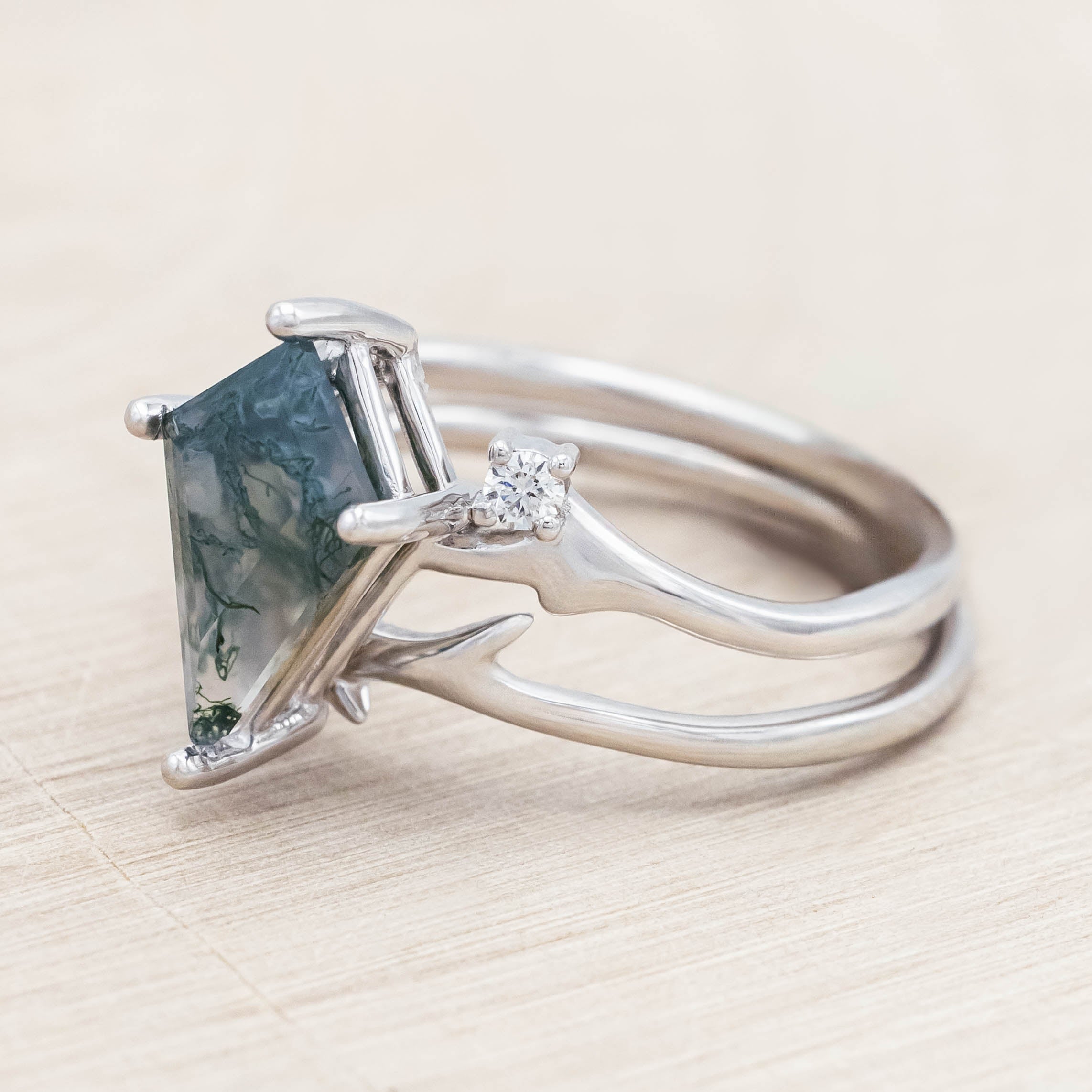 White gold ring with kite cut green moss agate on a light wood surface