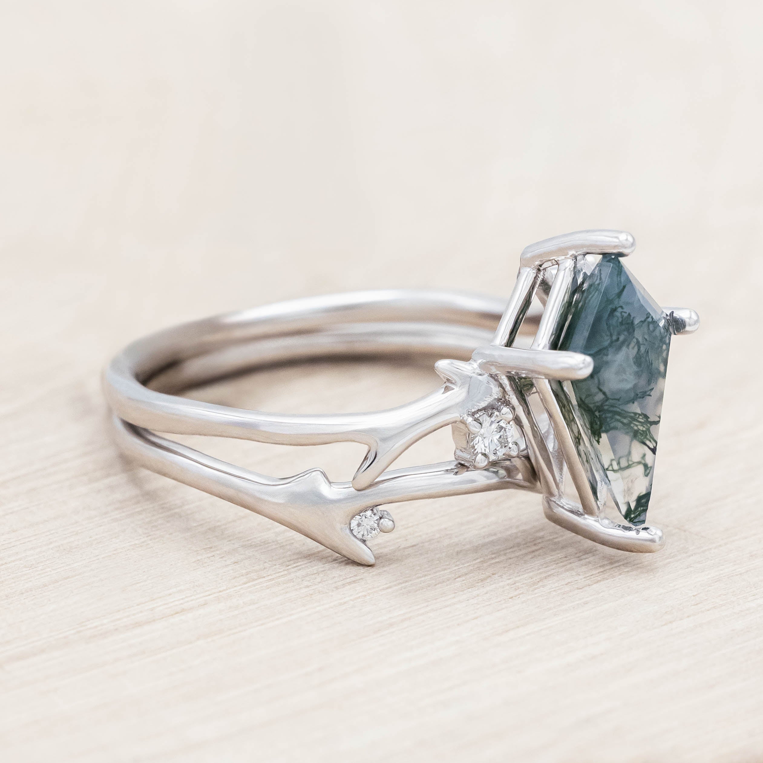 White gold ring with kite cut green moss agate on a light wood surface