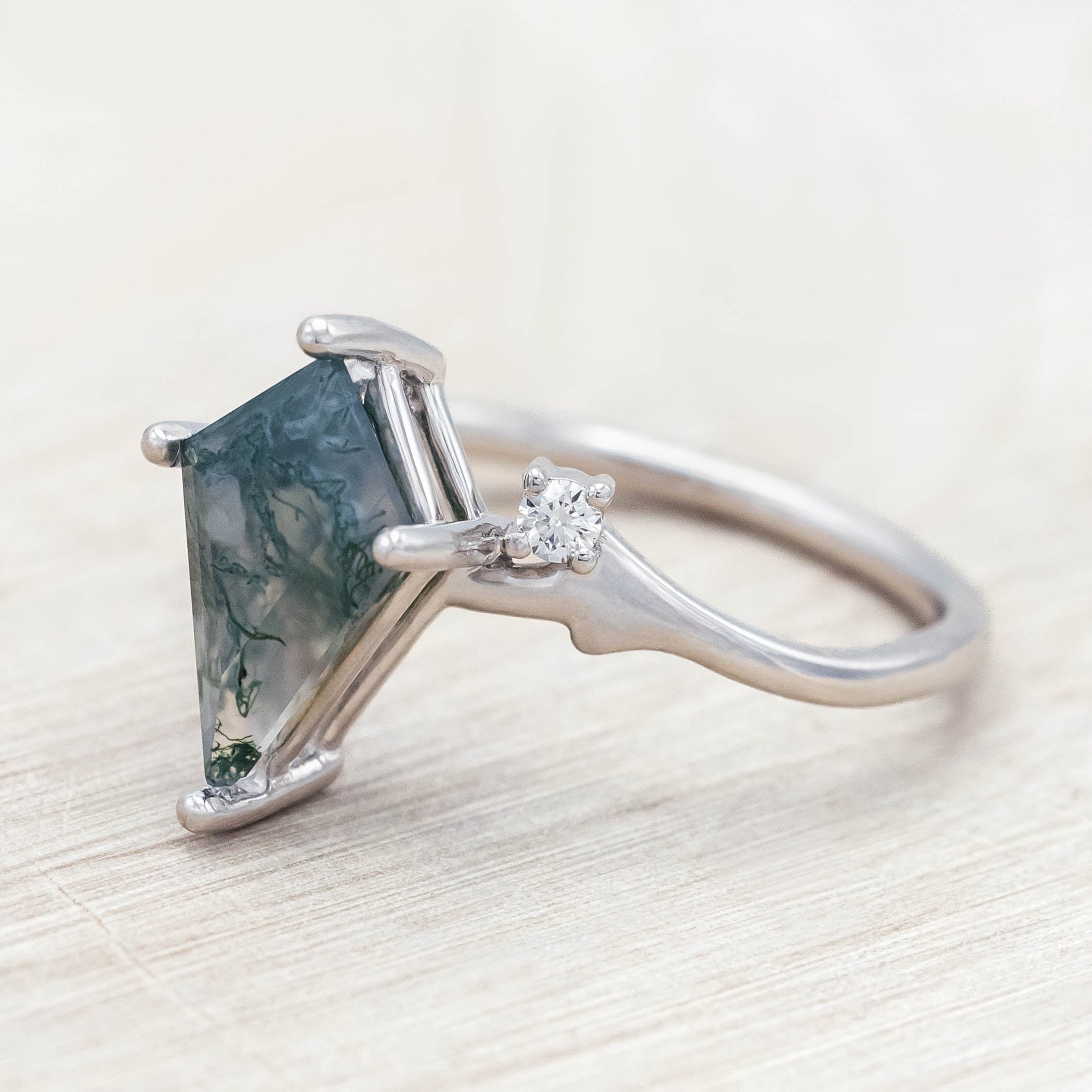 White gold ring with kite cut green moss agate on a light wood surface