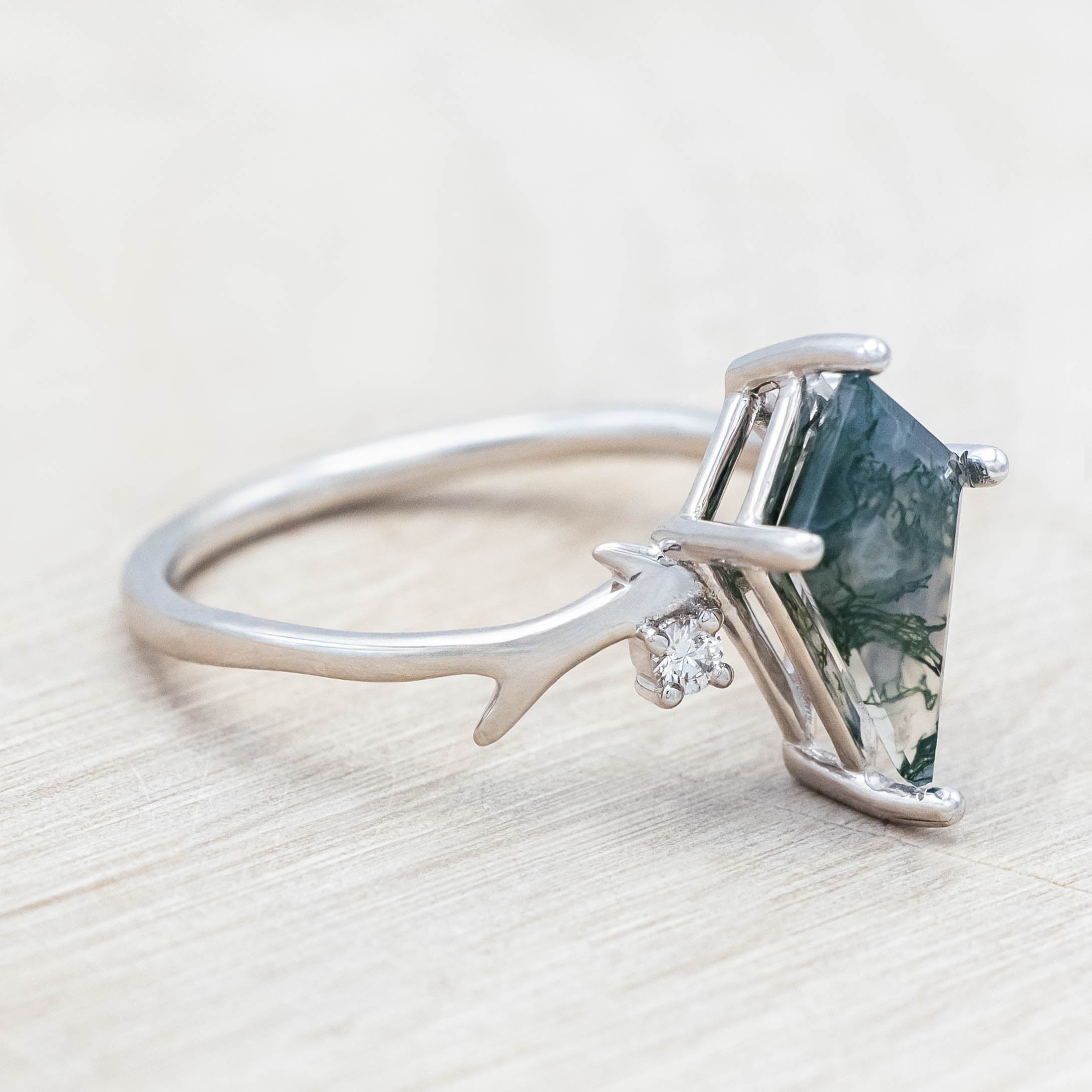 White gold ring with kite cut green moss agate on a light wood surface