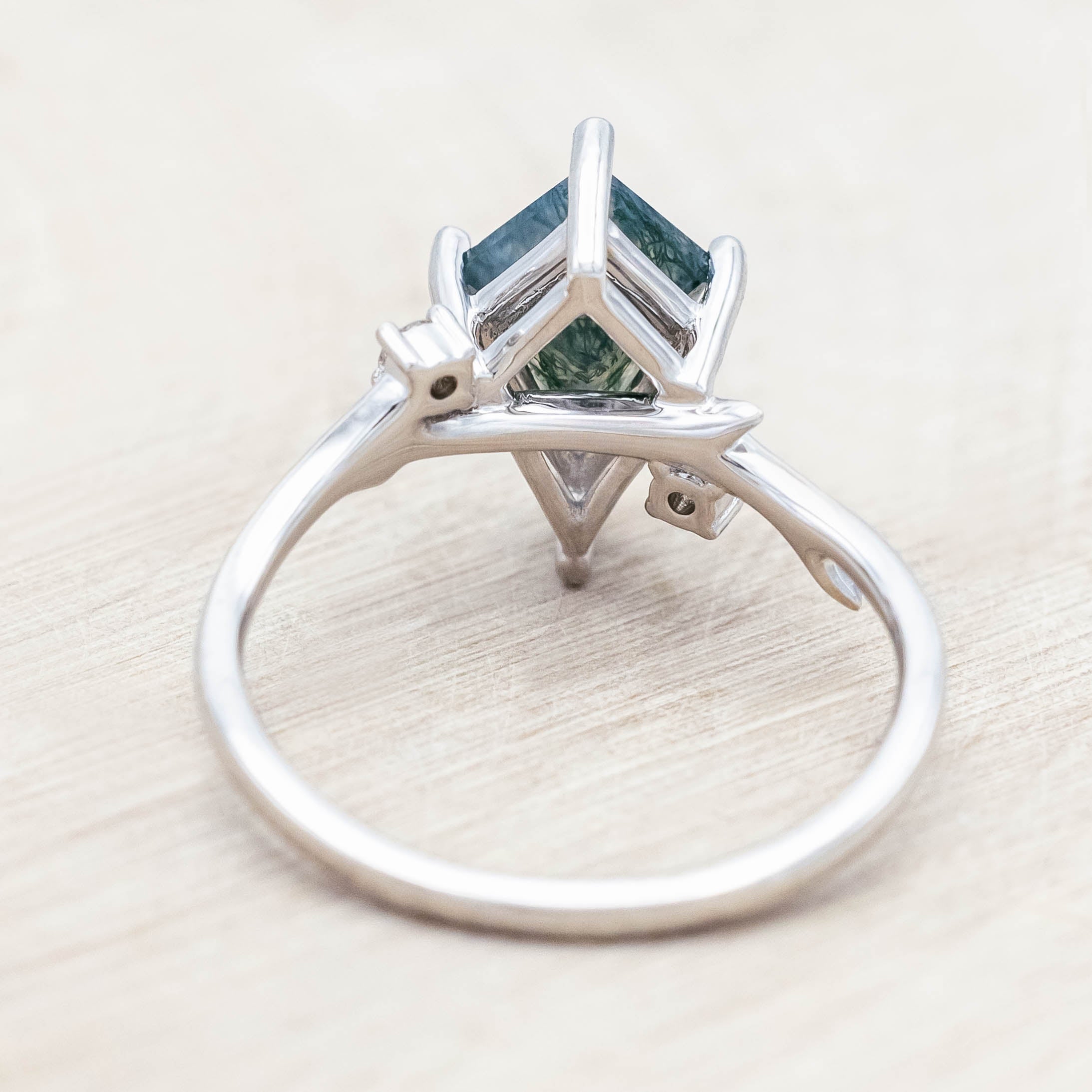 Backside of white gold ring with kite cut green moss agate on a light wood surface