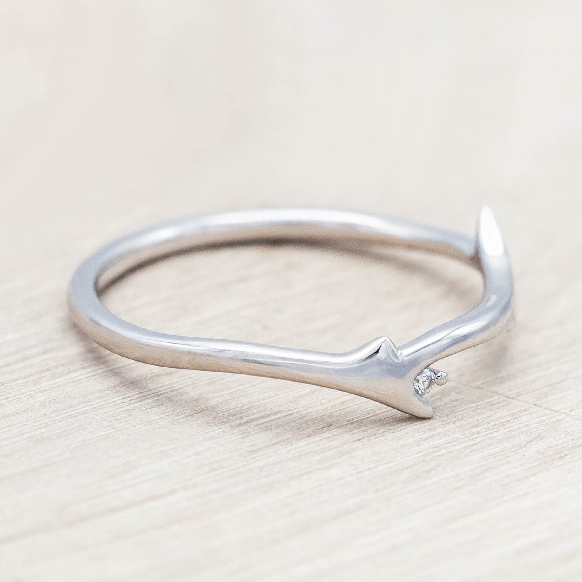 White gold ring with round diamond on a light wood background