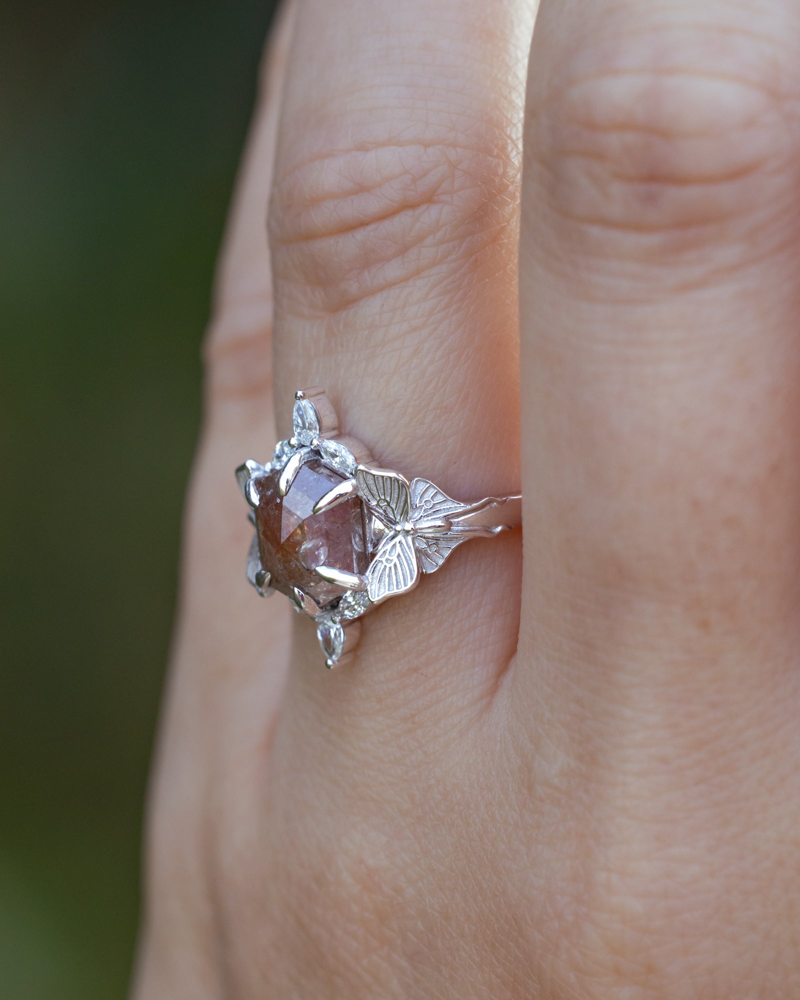White gold ring with a salt & pepper diamond on a finger against a blurred background