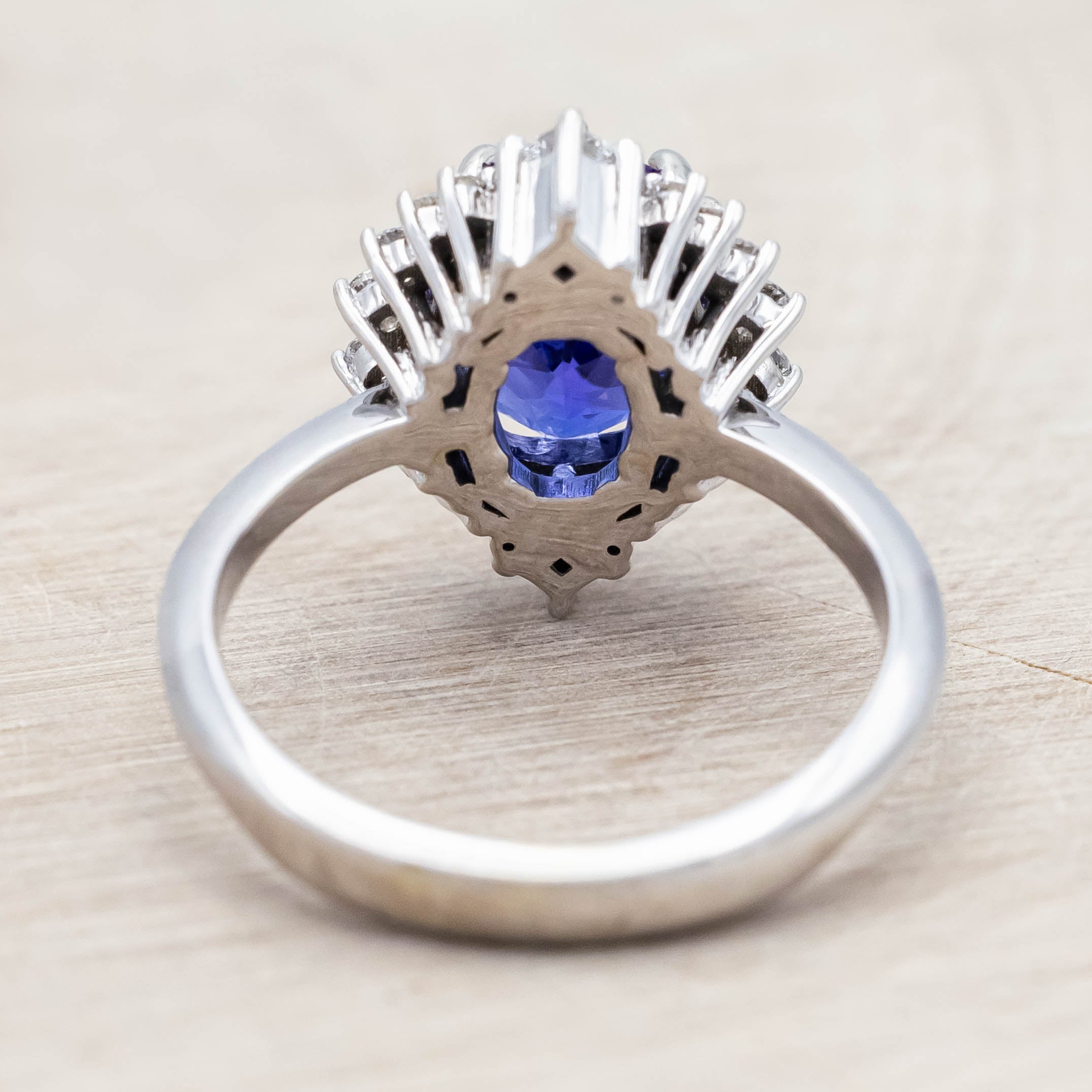 14K white gold ring with a blue tanzanite center stone and diamond halo on a beige background
