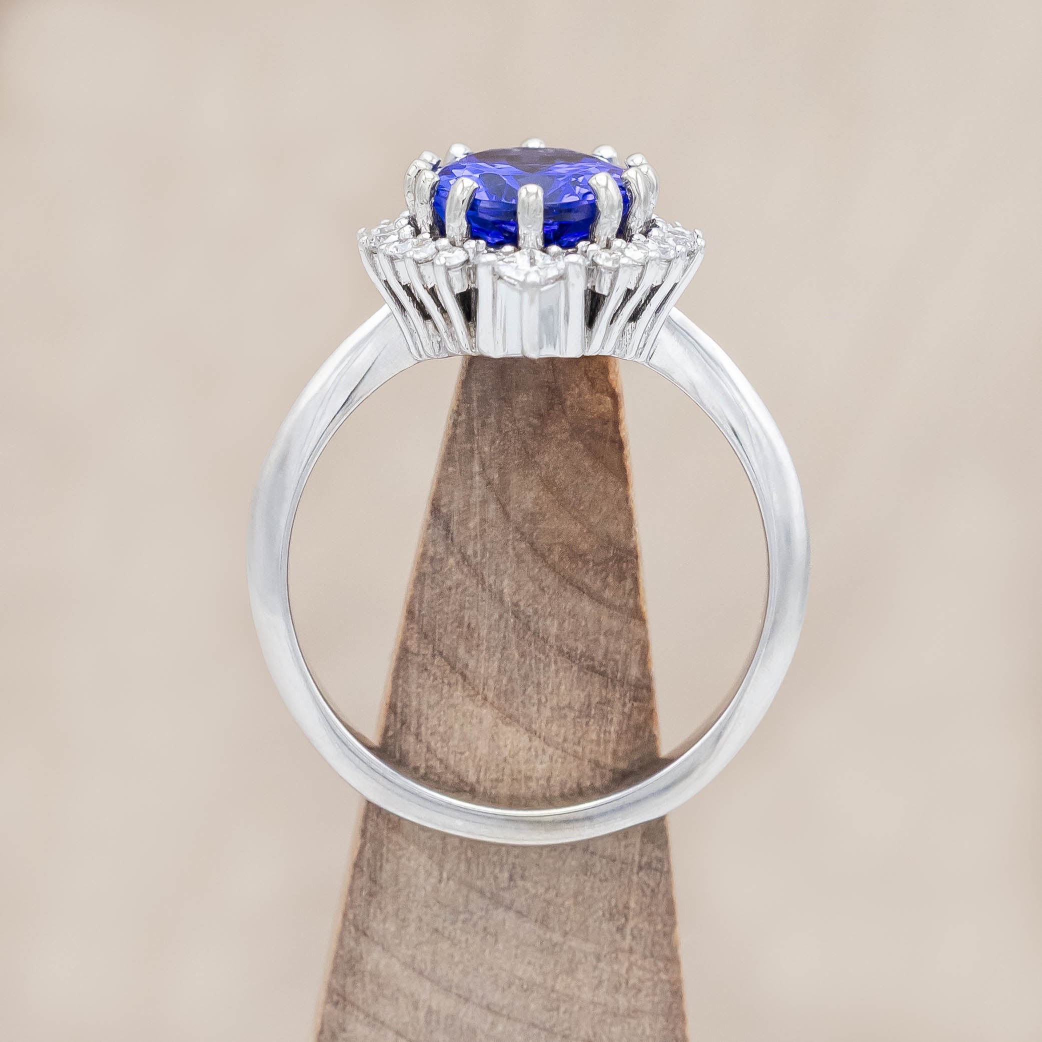 14K white gold ring with a blue tanzanite center stone and diamond halo on a beige background