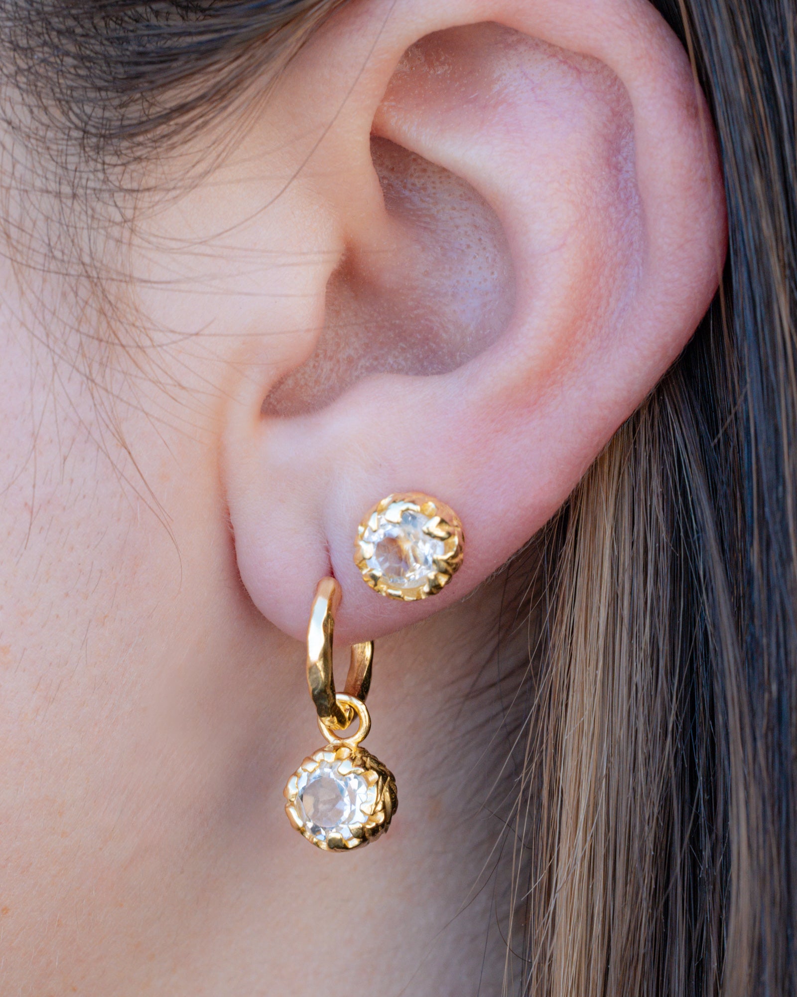 Close-up of an ear wearing gold hoop earrings with white topaz