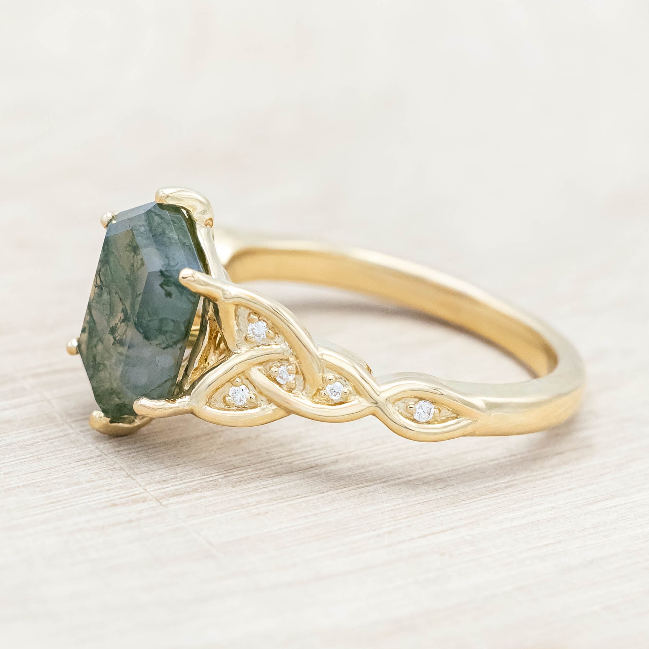 Gold ring with triquetra knot accent and moss agate on a light wooden background