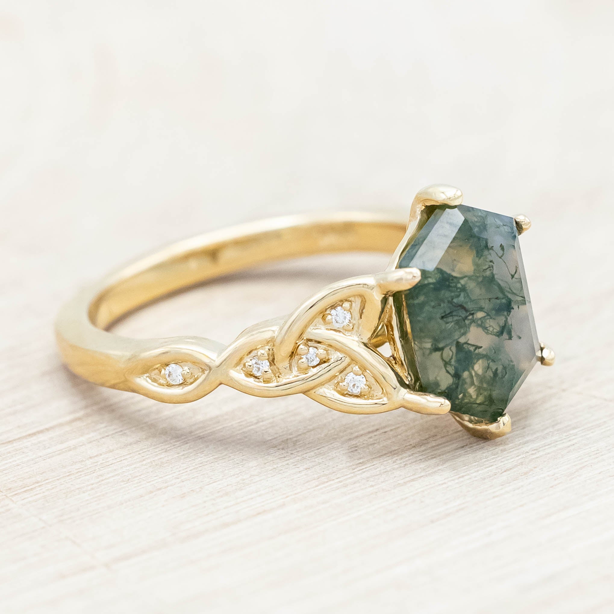 Gold ring with triquetra knot accent and moss agate on a light wooden background